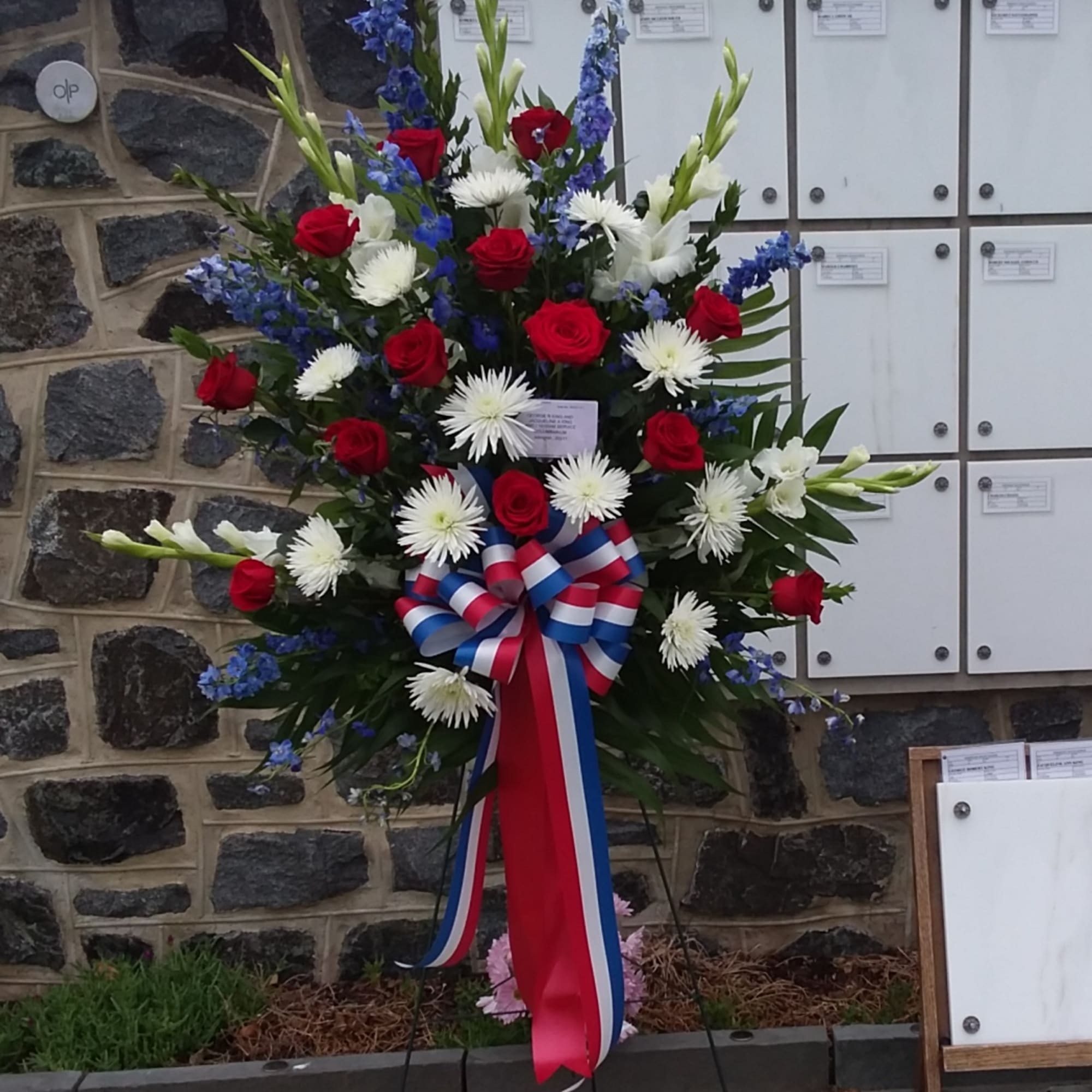 Standing floral spray with red roses, white daisies, and blue flowers on an easel