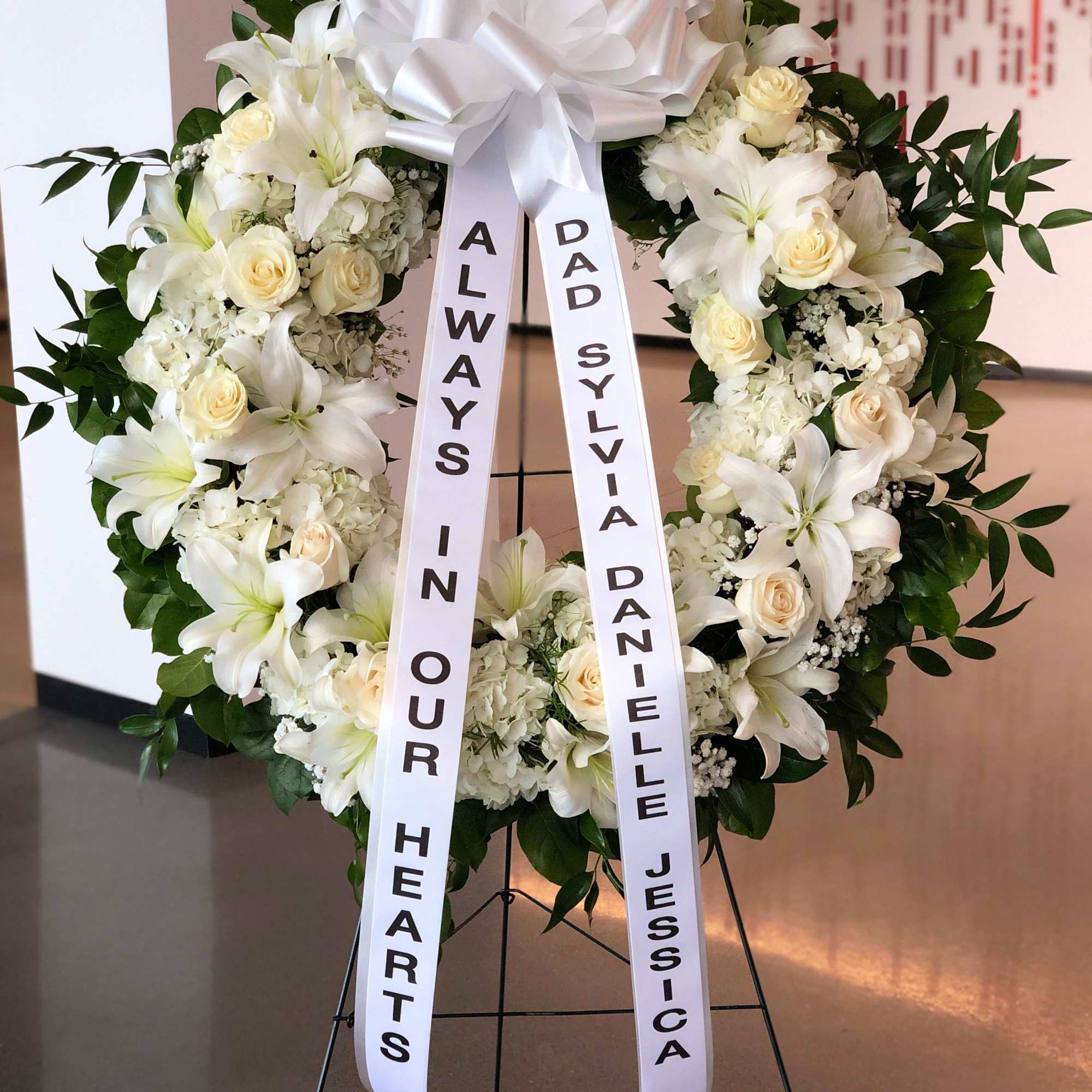 White funeral wreath with lilies and roses on a stand