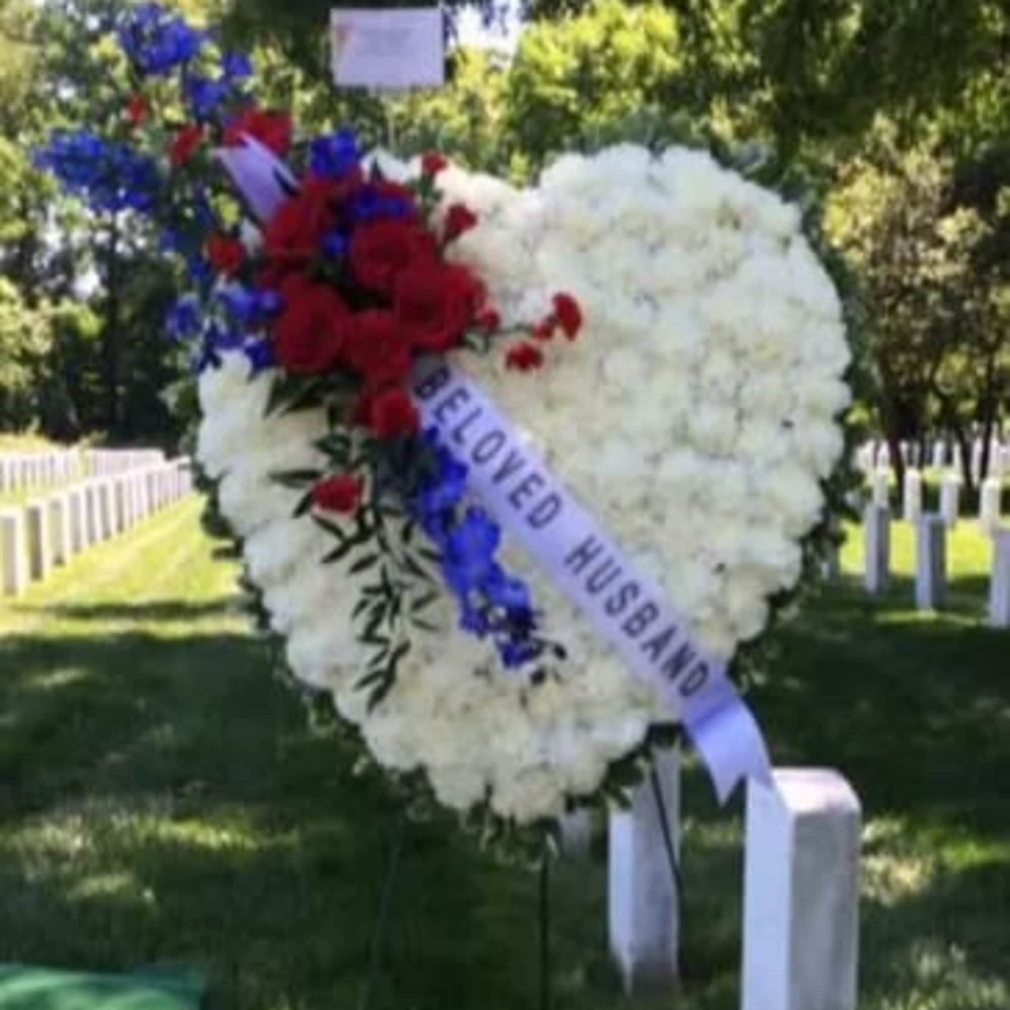 Heart-shaped funeral wreath with red, white, and blue flowers and a memorial ribbon