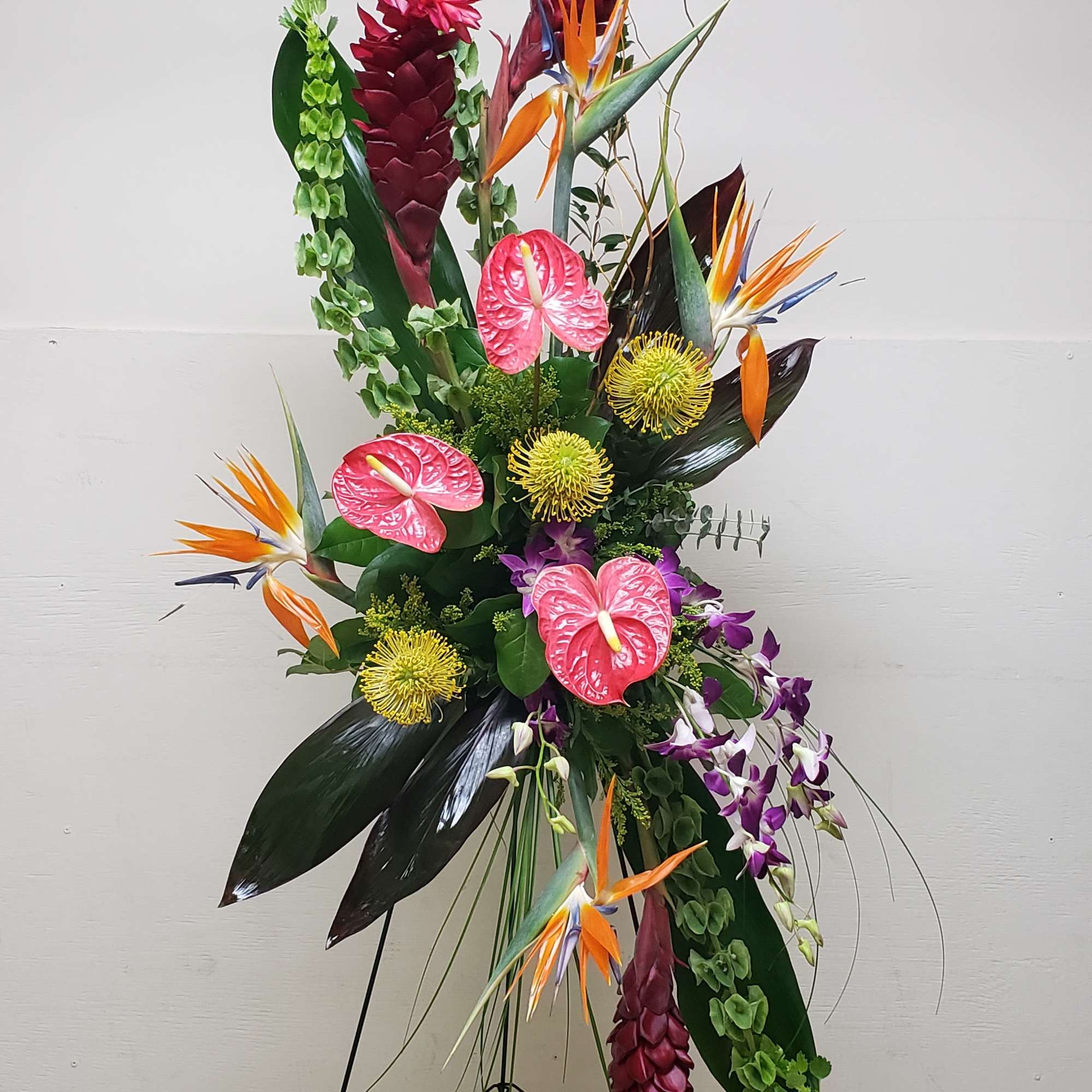 Tall tropical flower arrangement with orchids, anthuriums, and bird of paradise on a stand