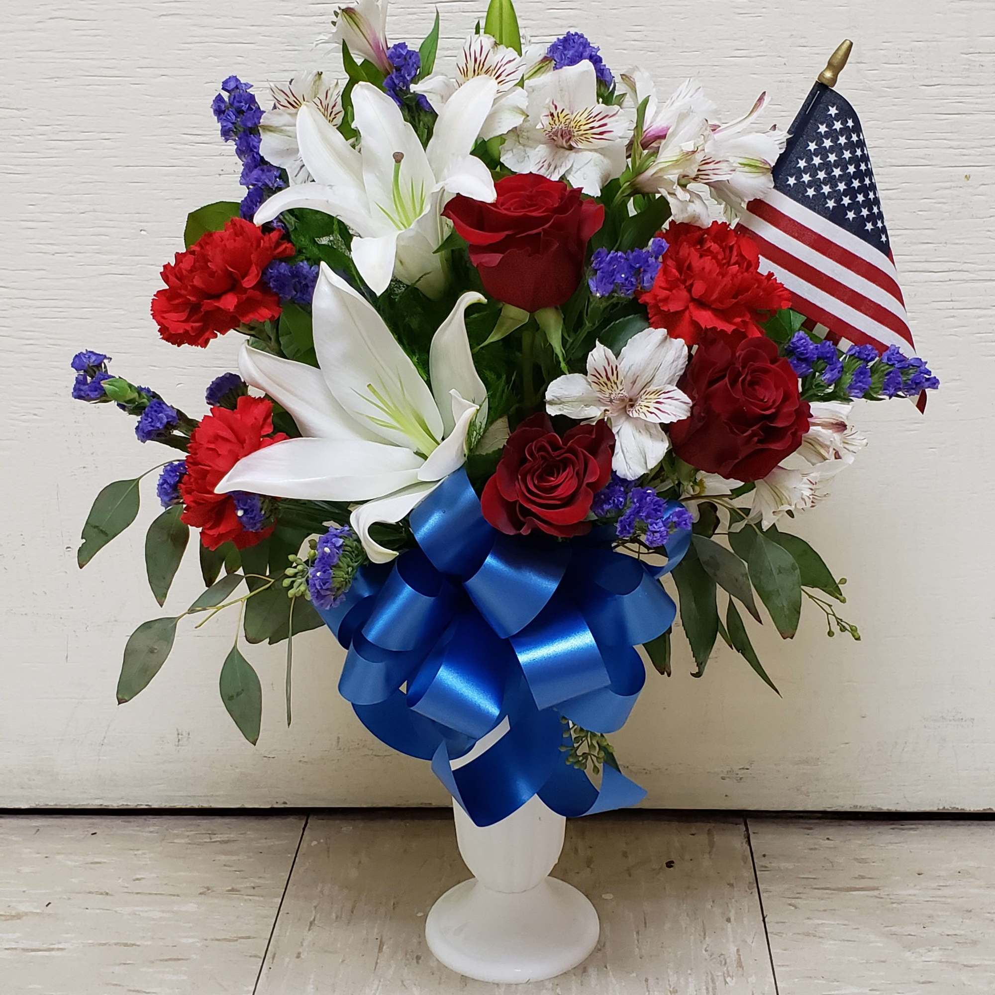 Red roses and white lilies in a white pedestal vase with a small American flag