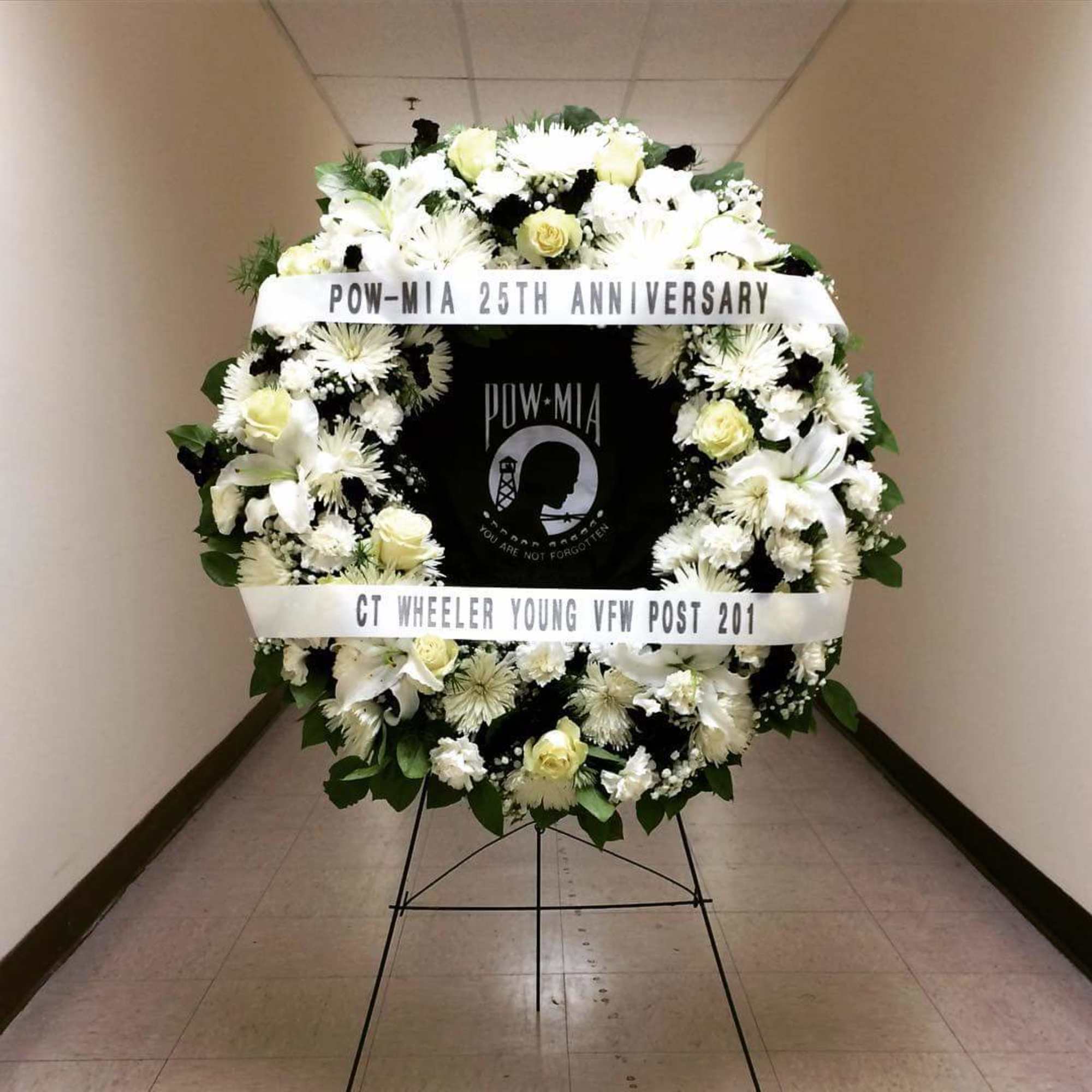 Large white funeral wreath on a stand with memorial ribbons
