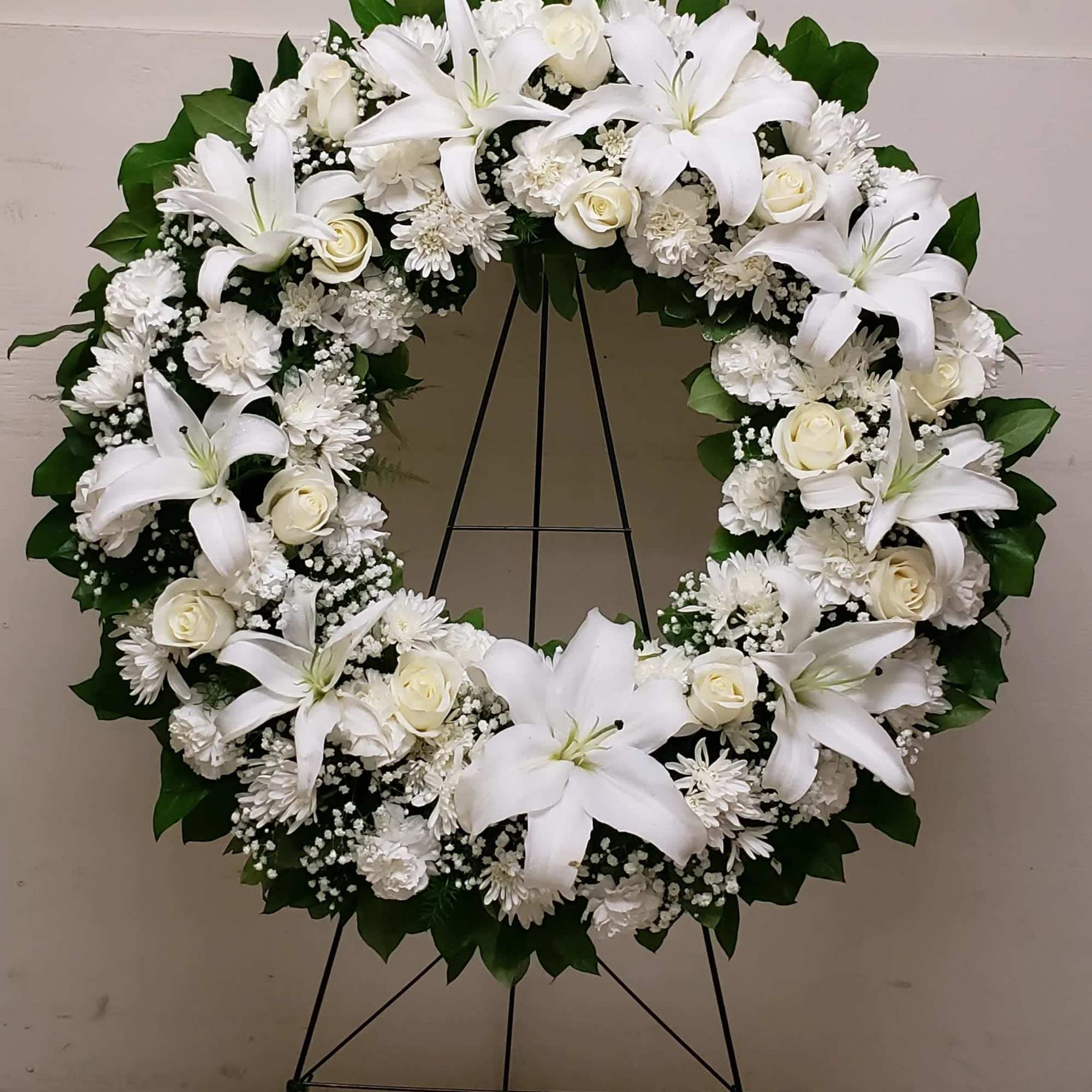 White floral wreath on a standing easel with lilies and roses