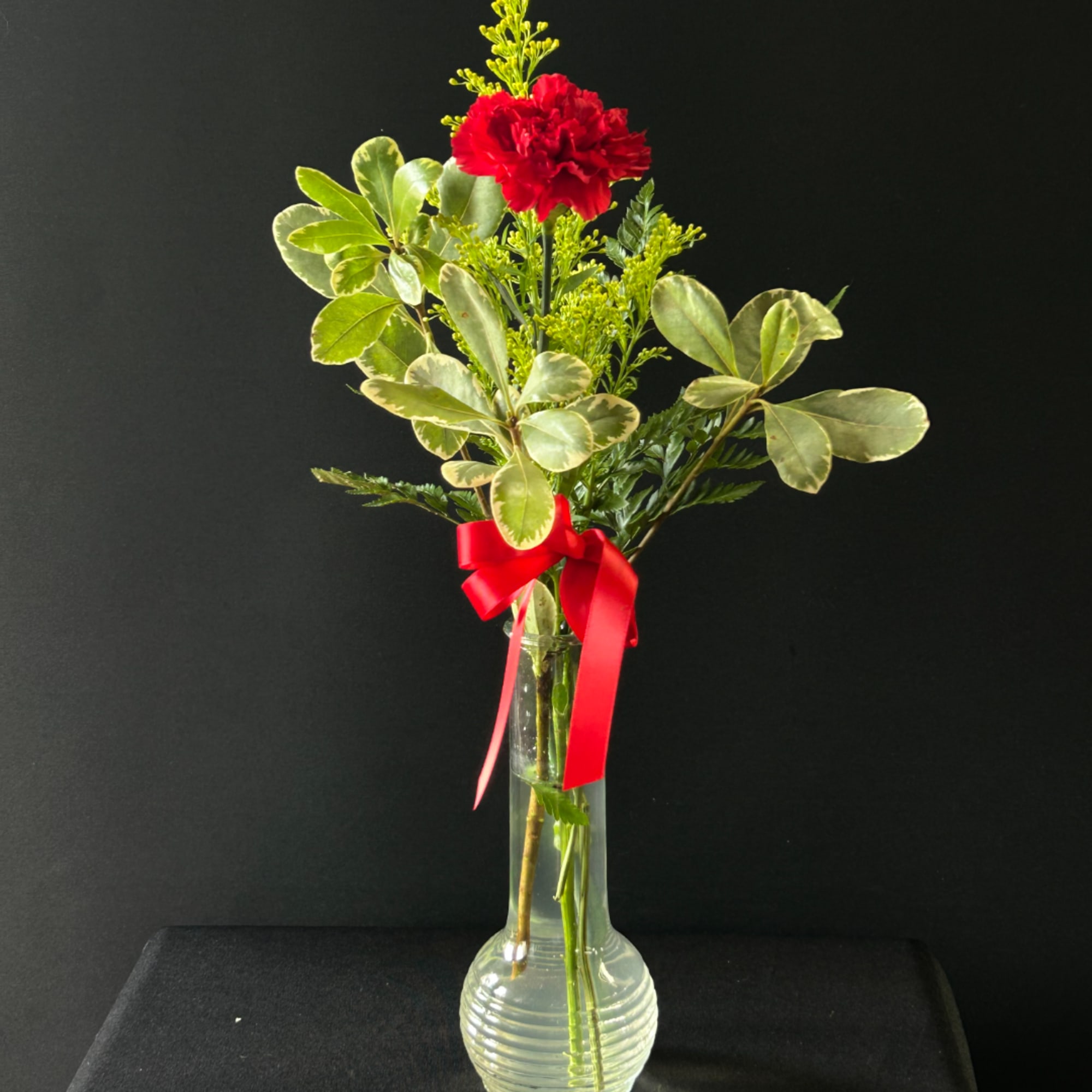 Red carnation arrangement in a clear glass vase with a red ribbon
