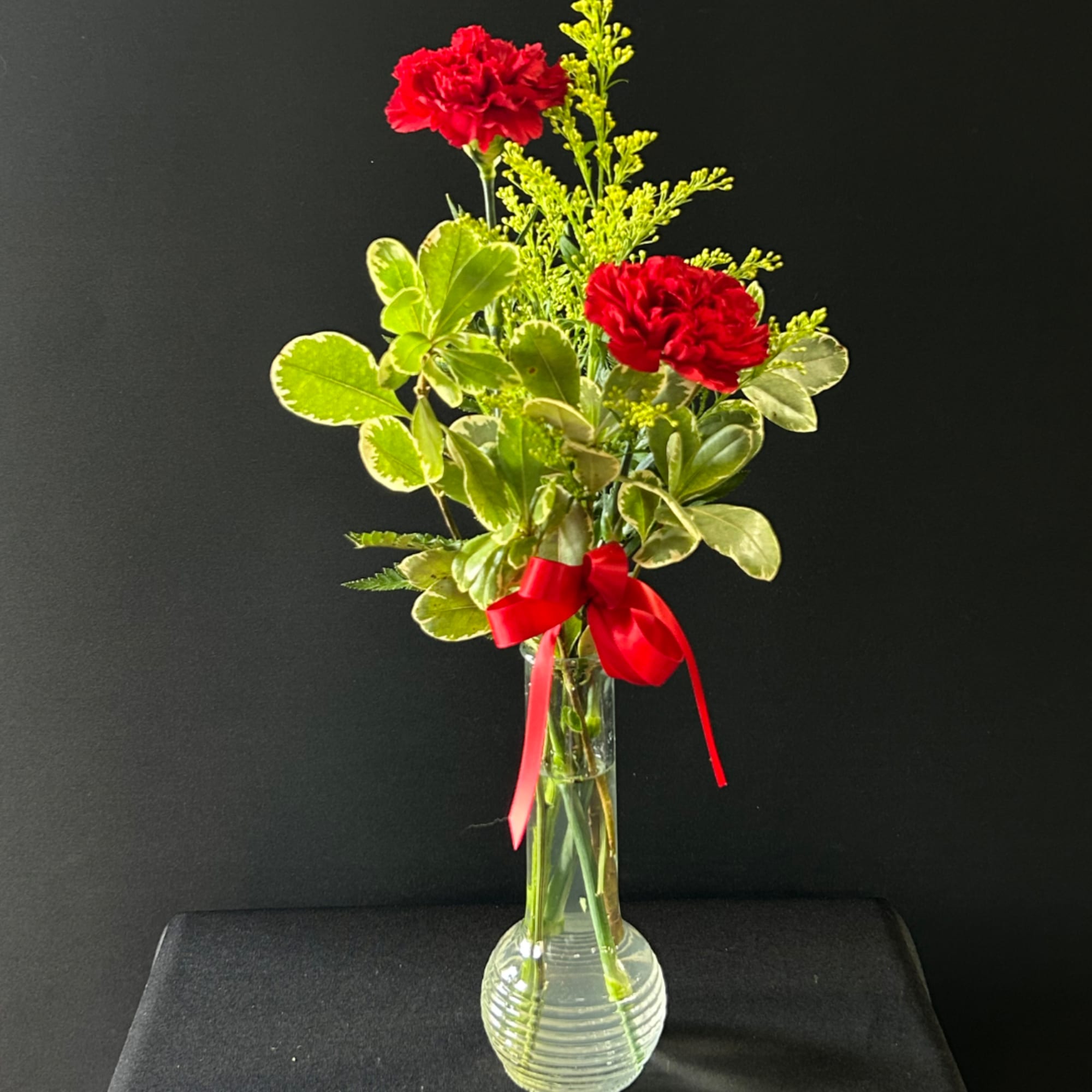 Red carnations in a clear glass vase with a red ribbon