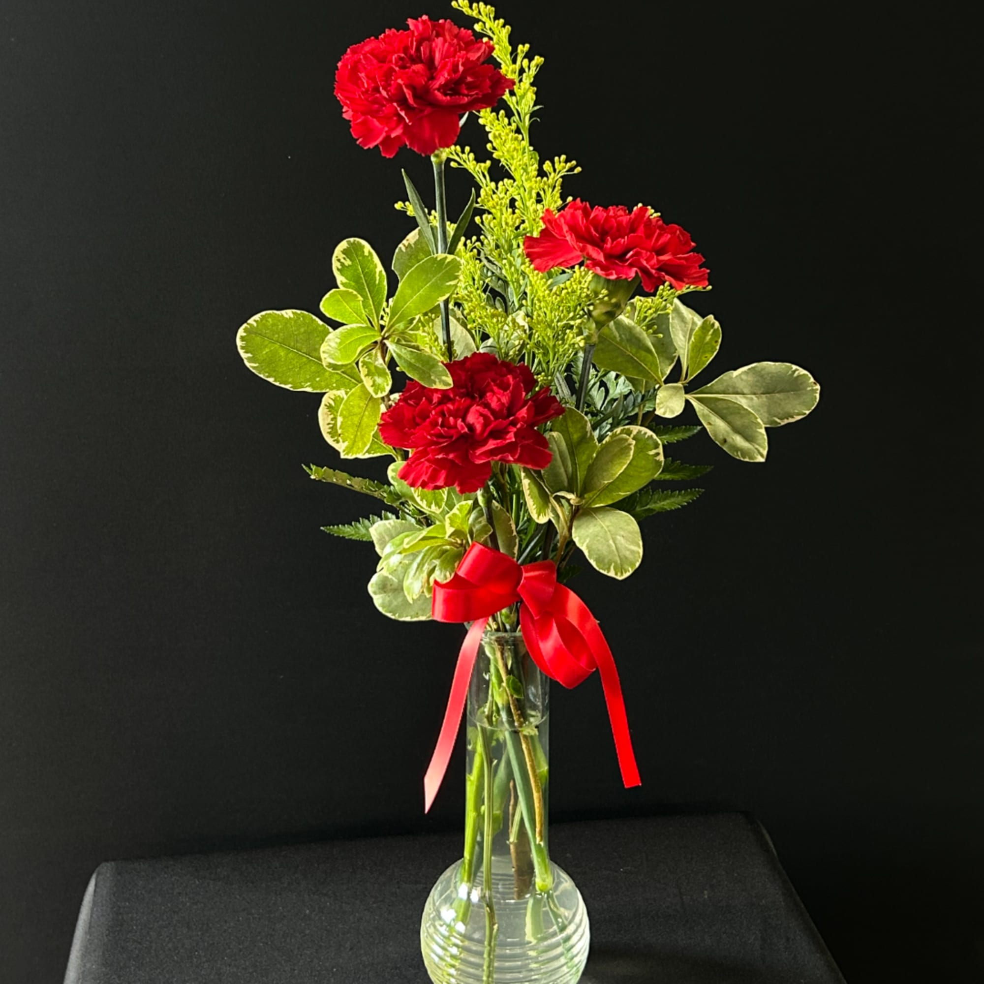 Red carnations in a clear glass vase with a red ribbon
