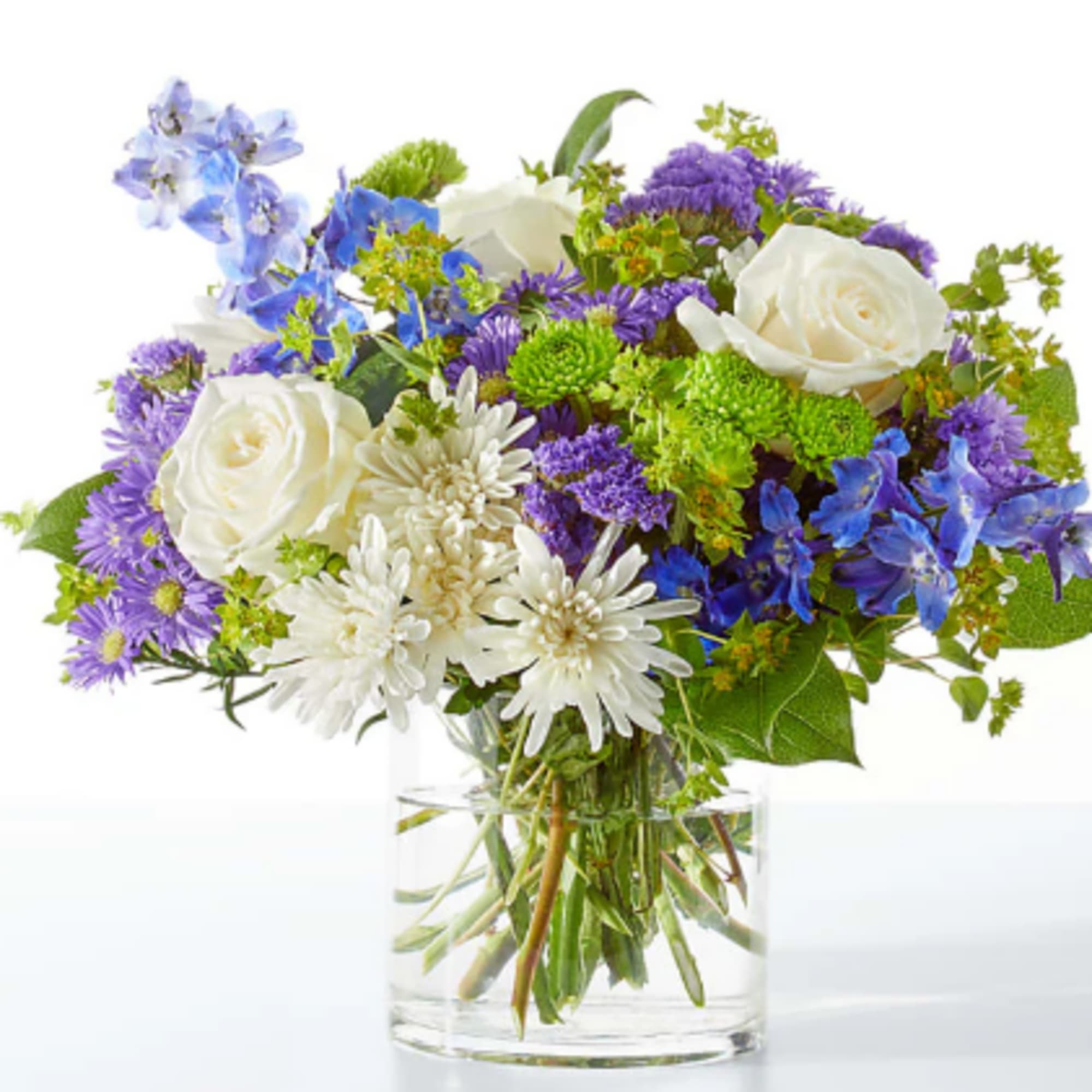 Bouquet of white roses, purple blooms, and blue flowers in a clear glass vase