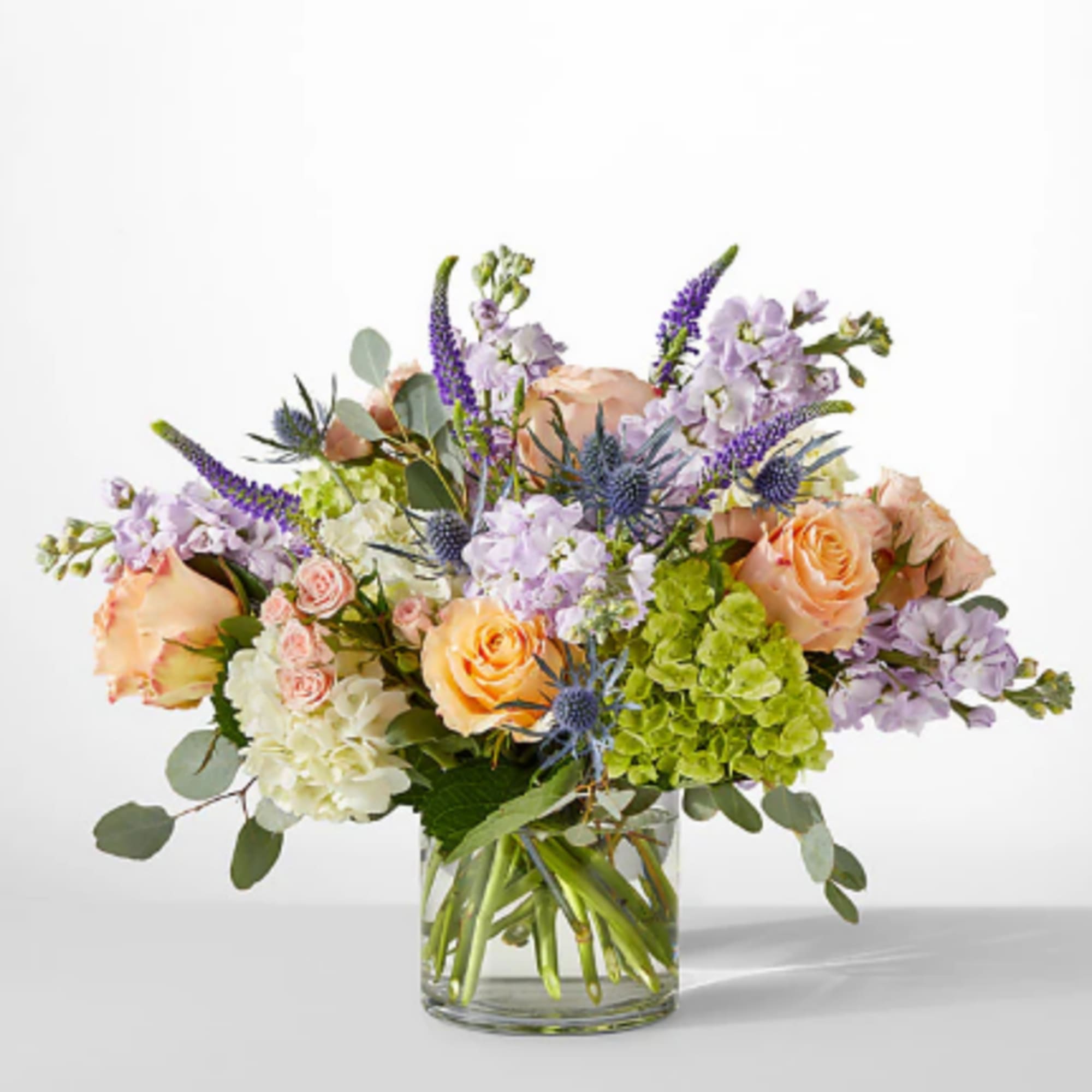 Mixed bouquet of peach roses, lavender blooms, and green hydrangeas in a glass vase