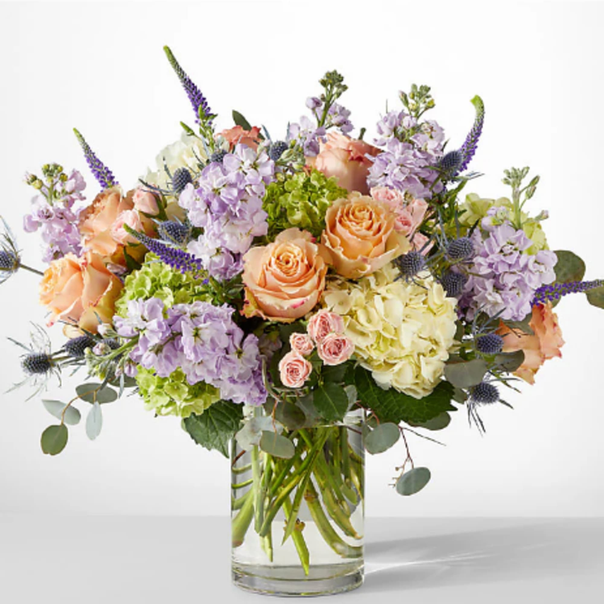Mixed bouquet of peach roses, lavender blooms, and hydrangeas in a glass vase