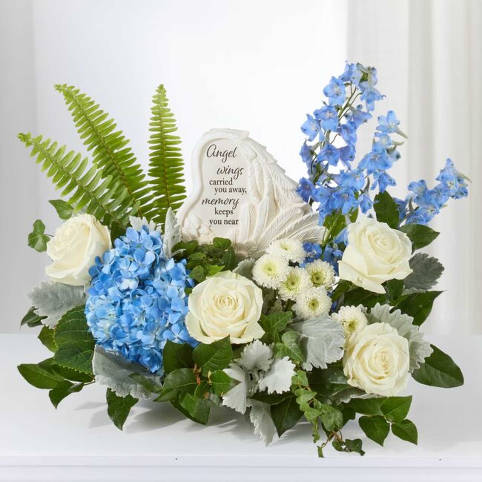White roses and blue flowers arranged around a memorial stone