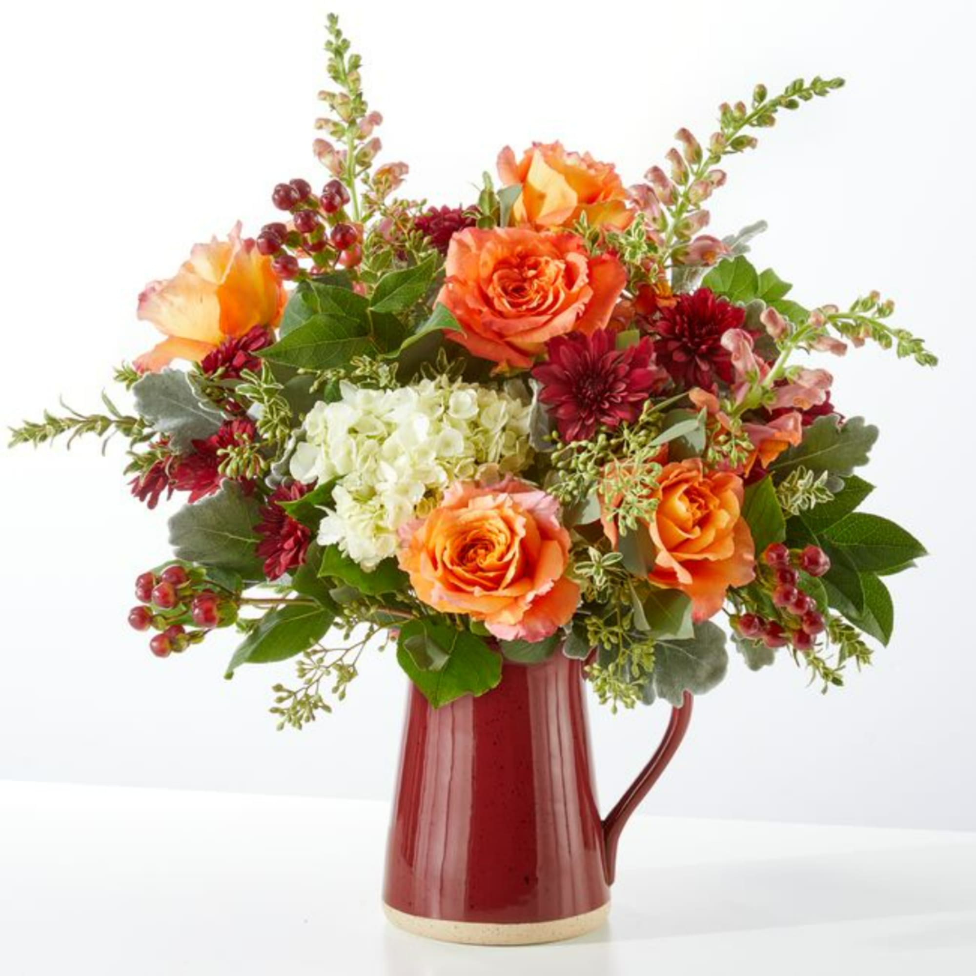 Orange roses and burgundy mums in a red ceramic pitcher vase