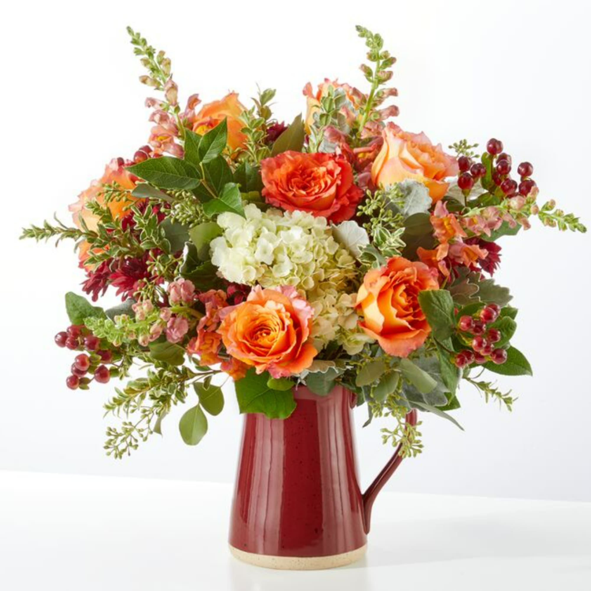 Orange roses and white hydrangea in a red ceramic pitcher vase