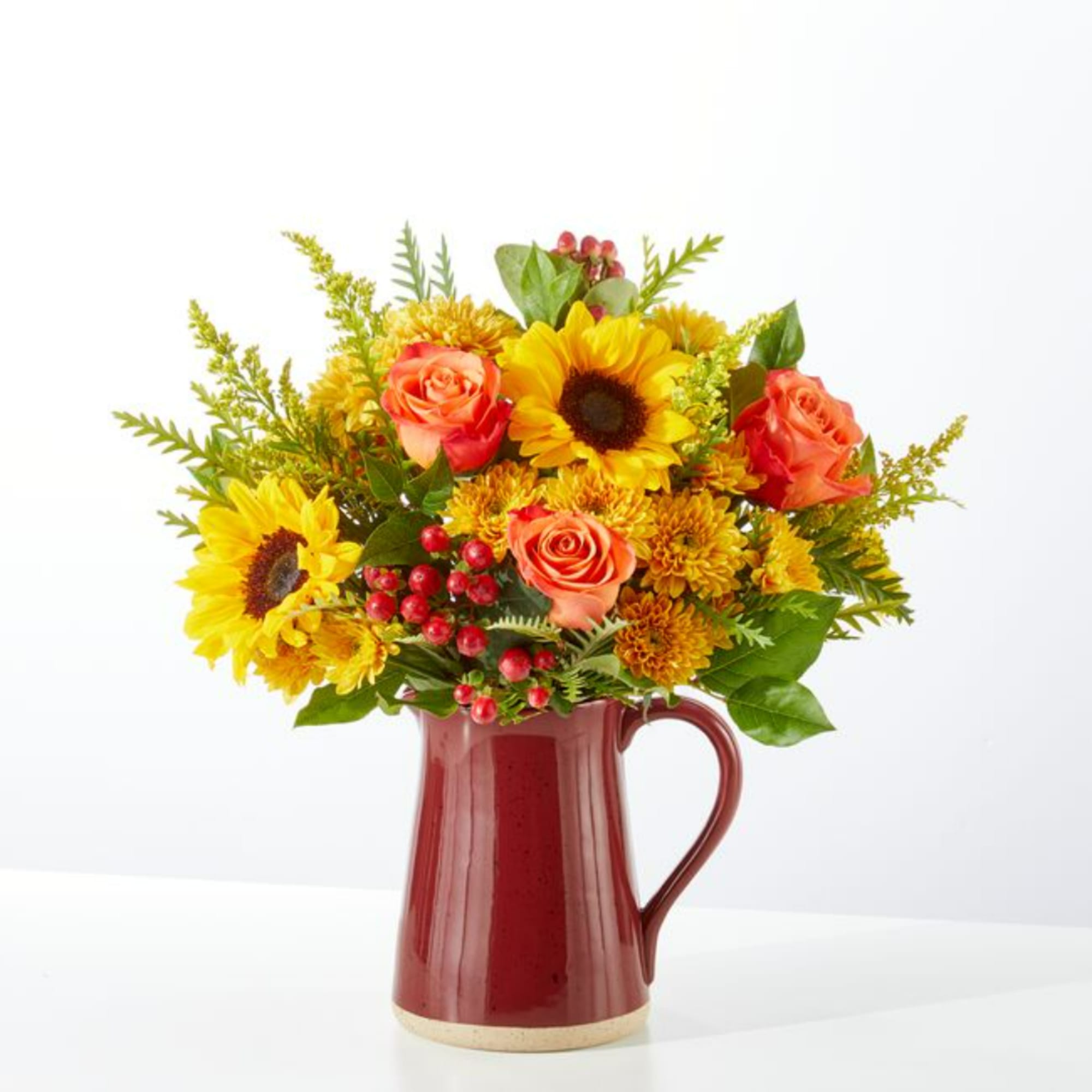 Sunflower and orange rose arrangement in a red ceramic pitcher