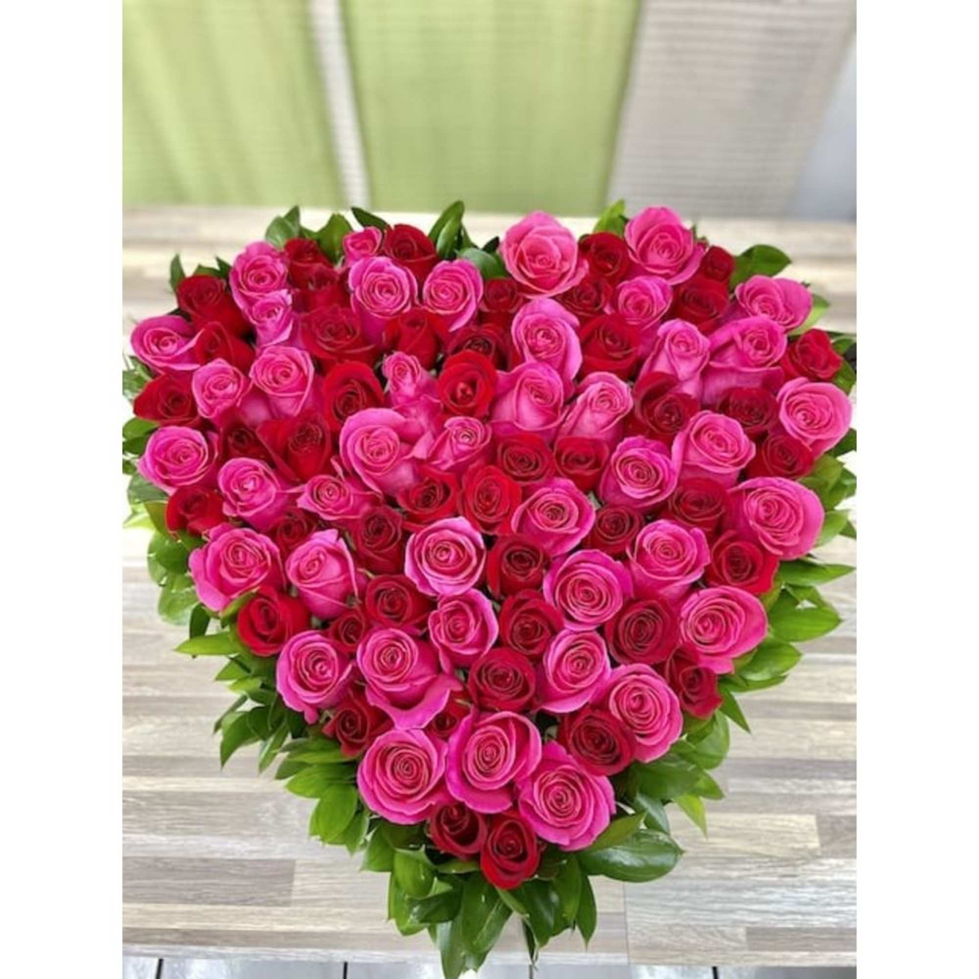Heart-shaped arrangement of red and hot pink roses bordered with green foliage.