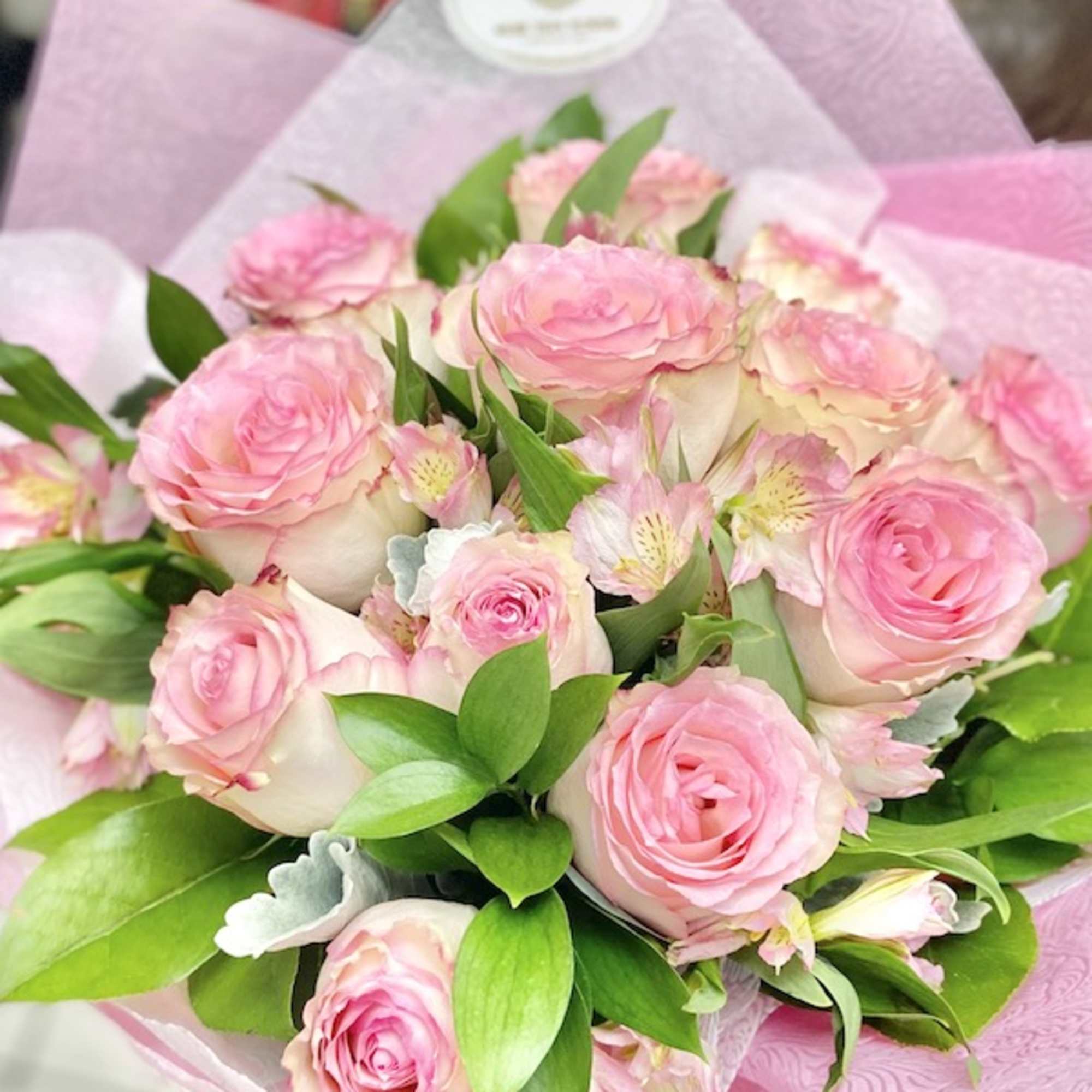 Hand-tied bouquet of pink roses and pale pink blooms wrapped in pink paper
