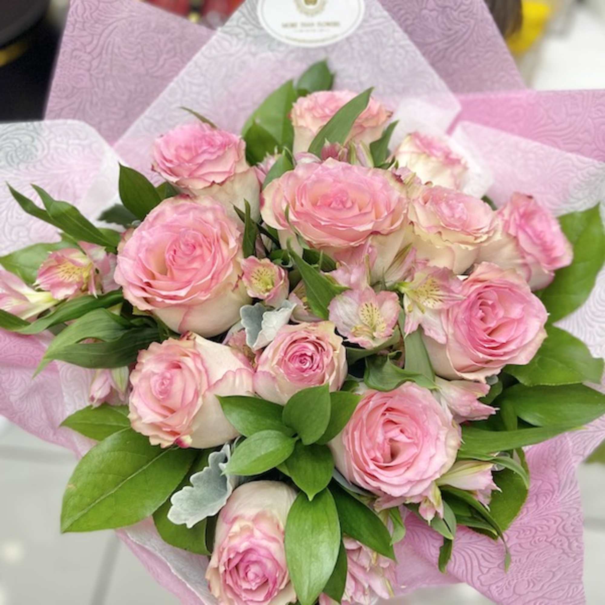 Hand-tied bouquet of pink roses with small accent flowers wrapped in pink patterned paper