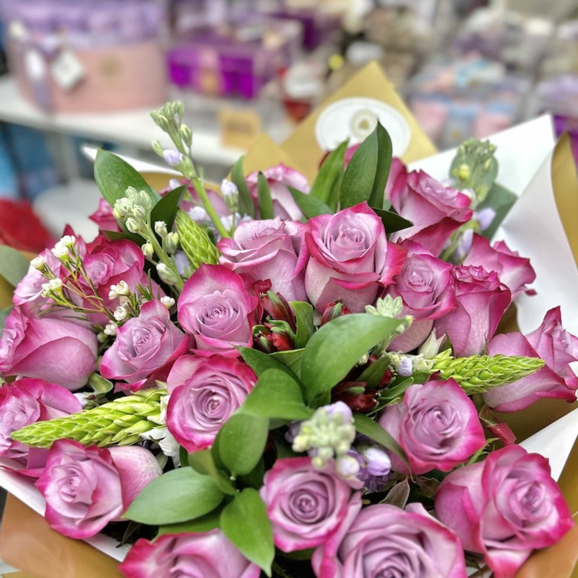 Hand-tied bouquet of pink and lavender roses with accent blooms wrapped in white and gold paper