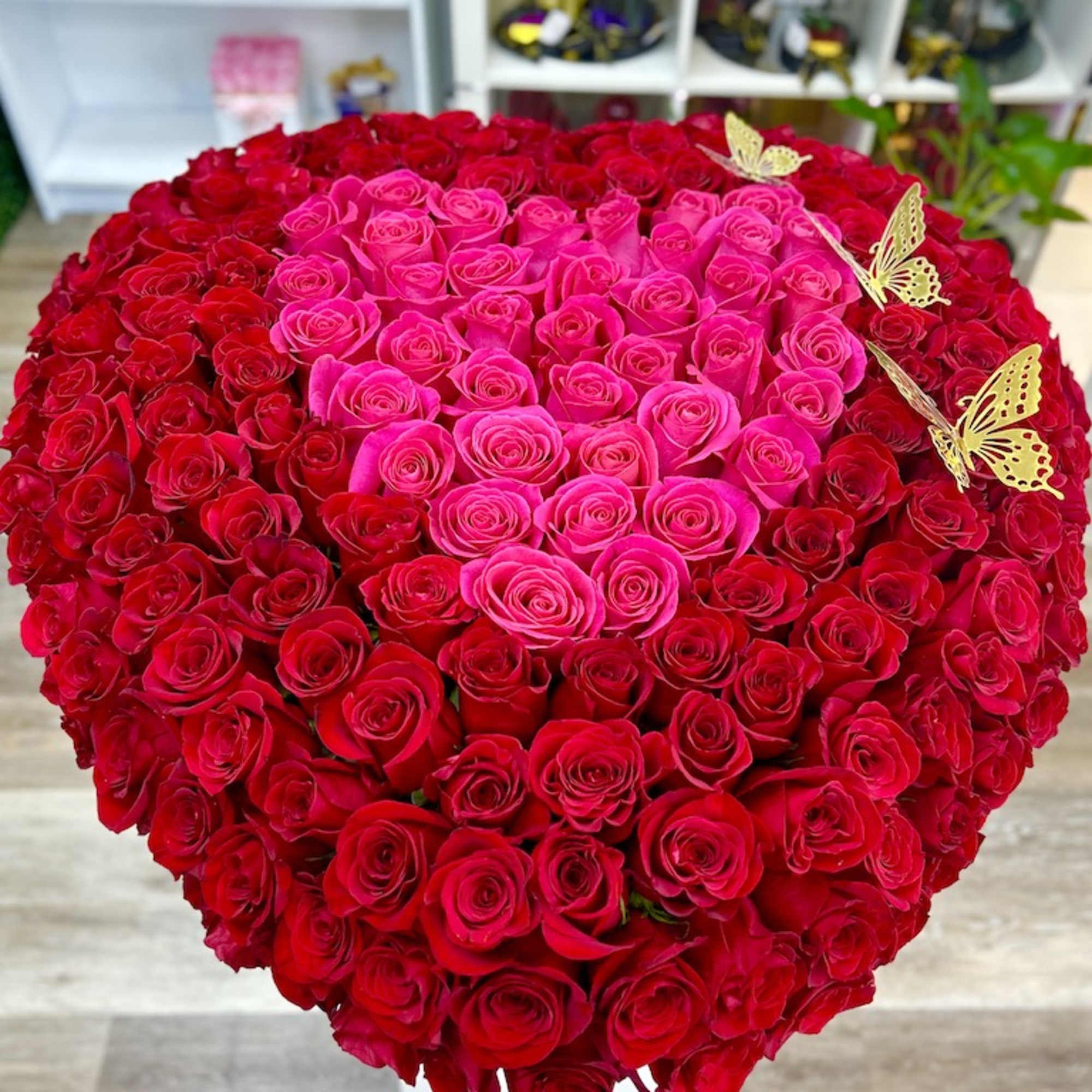 Heart-shaped arrangement of red roses with a central pink rose heart and gold butterfly accents.