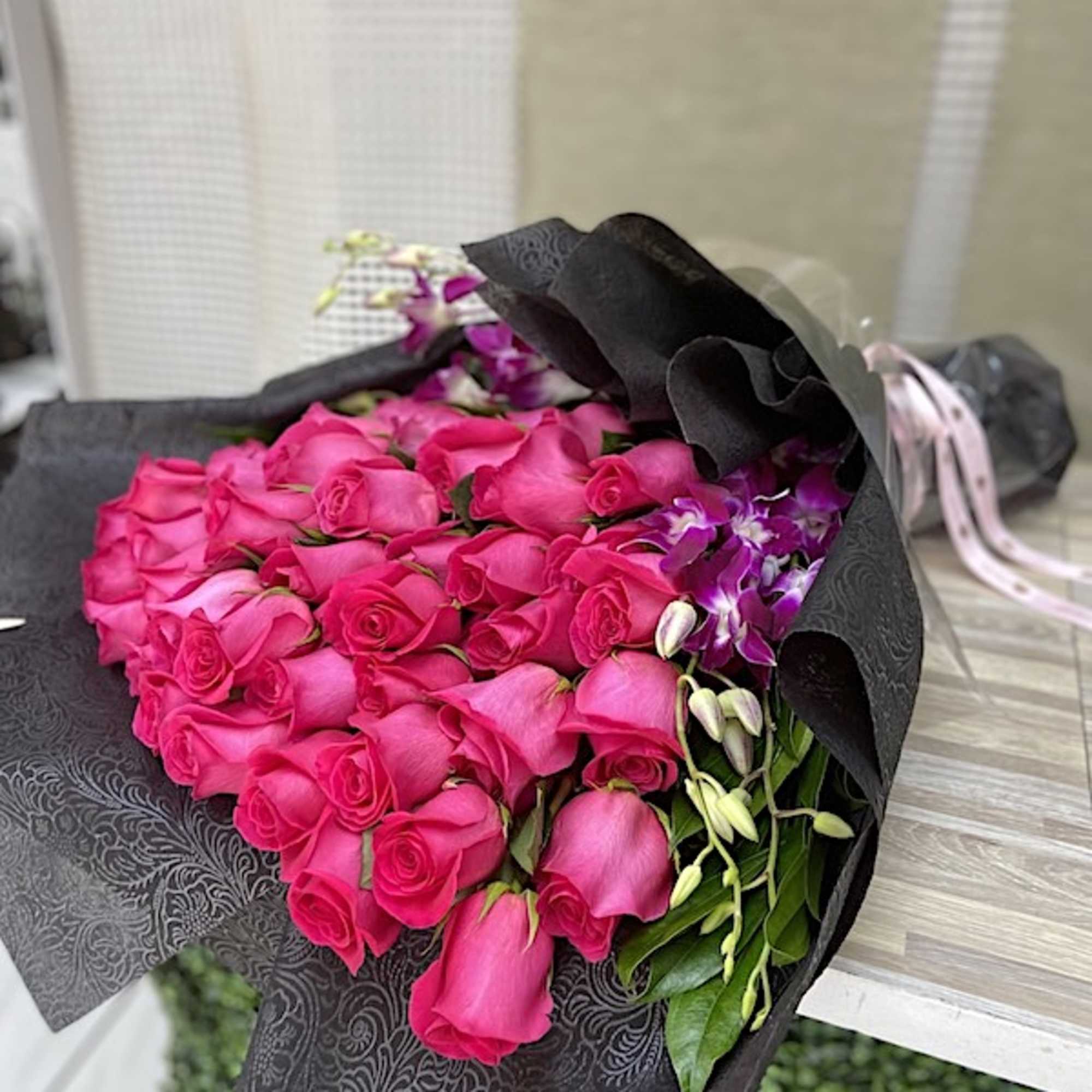 Large bouquet of hot pink roses and purple blooms wrapped in embossed black paper with ribbon