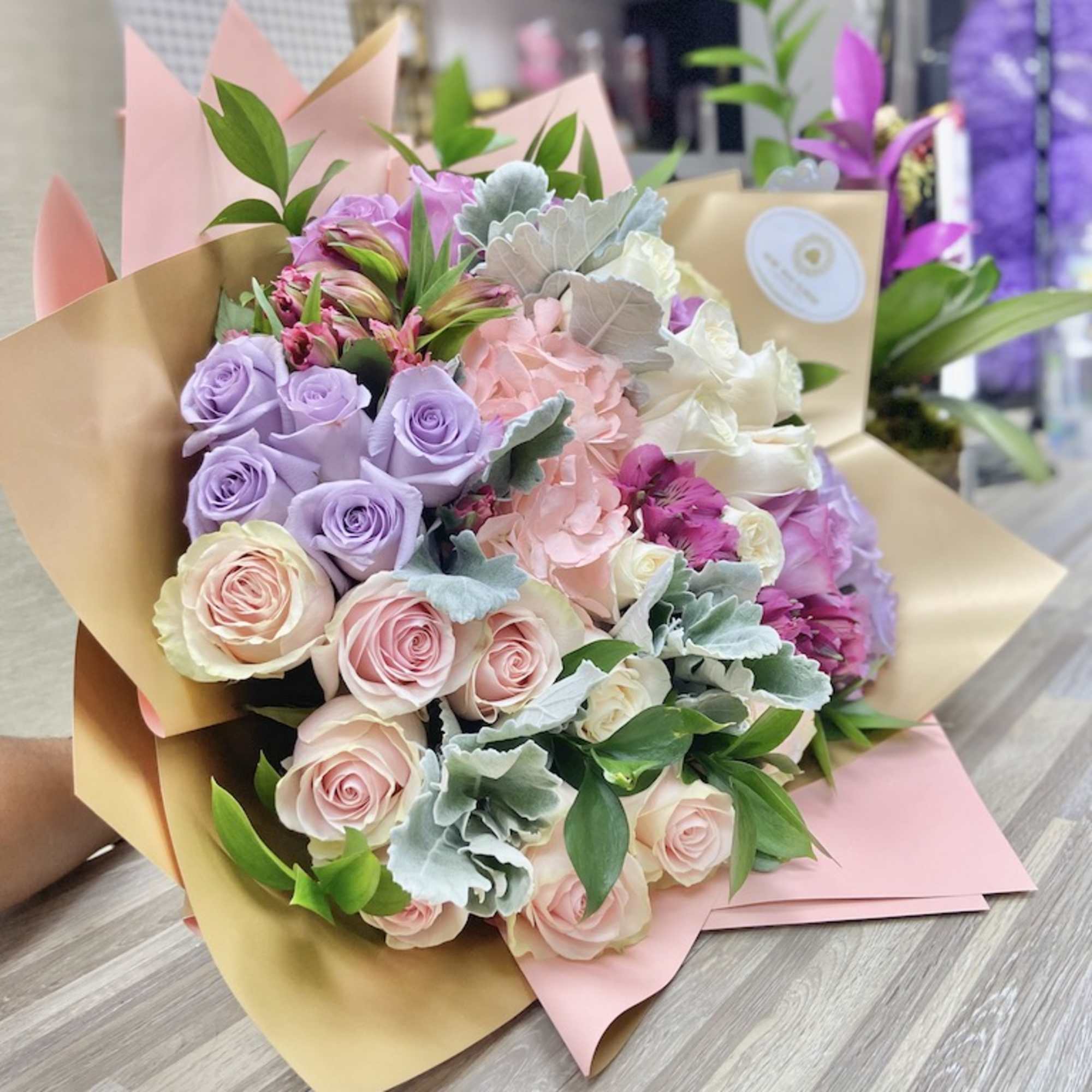 Hand-tied bouquet of pastel roses, hydrangea, and alstroemeria wrapped in tan and pink paper