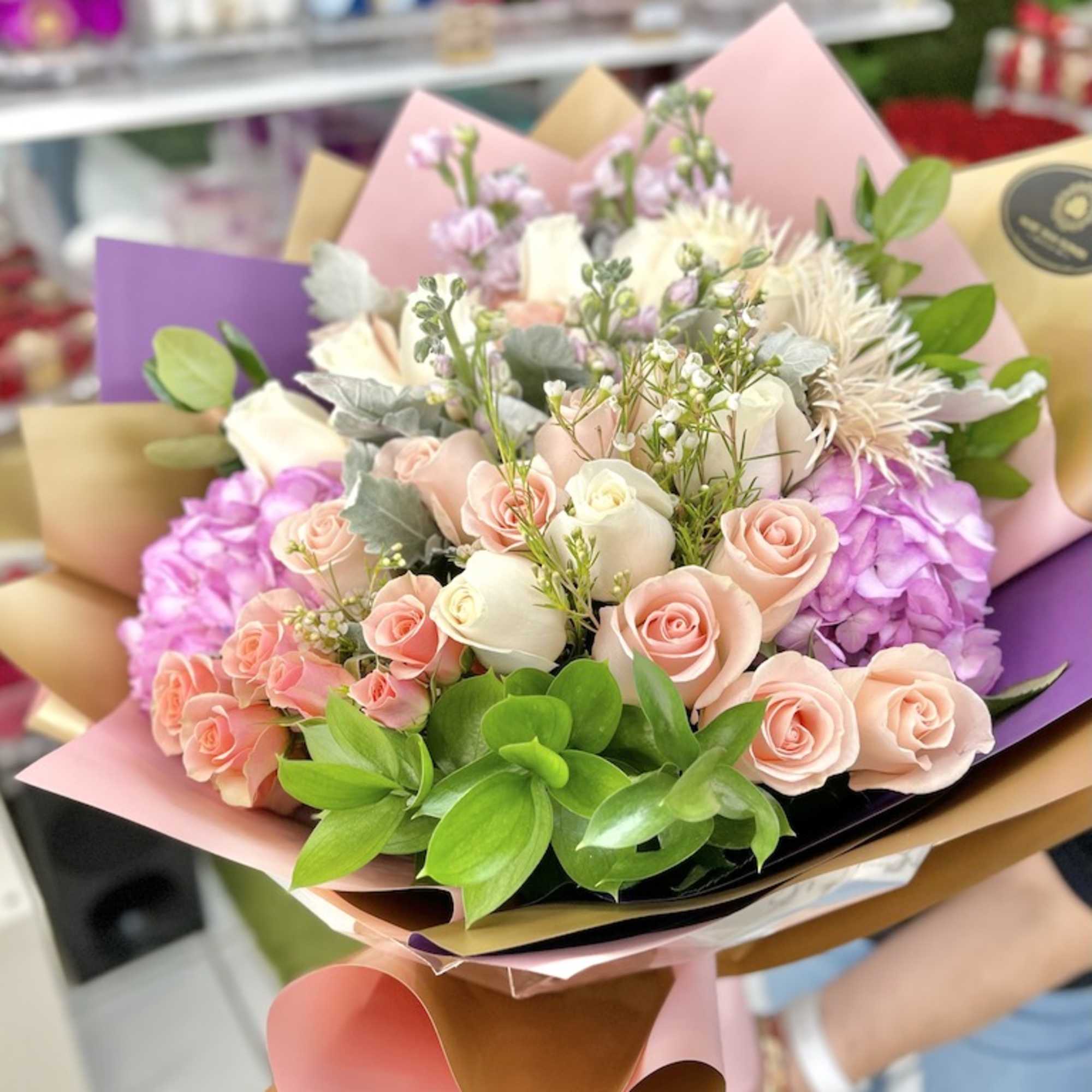 Hand-tied bouquet of pink and cream roses with hydrangeas and mixed blooms in pastel wrapping paper