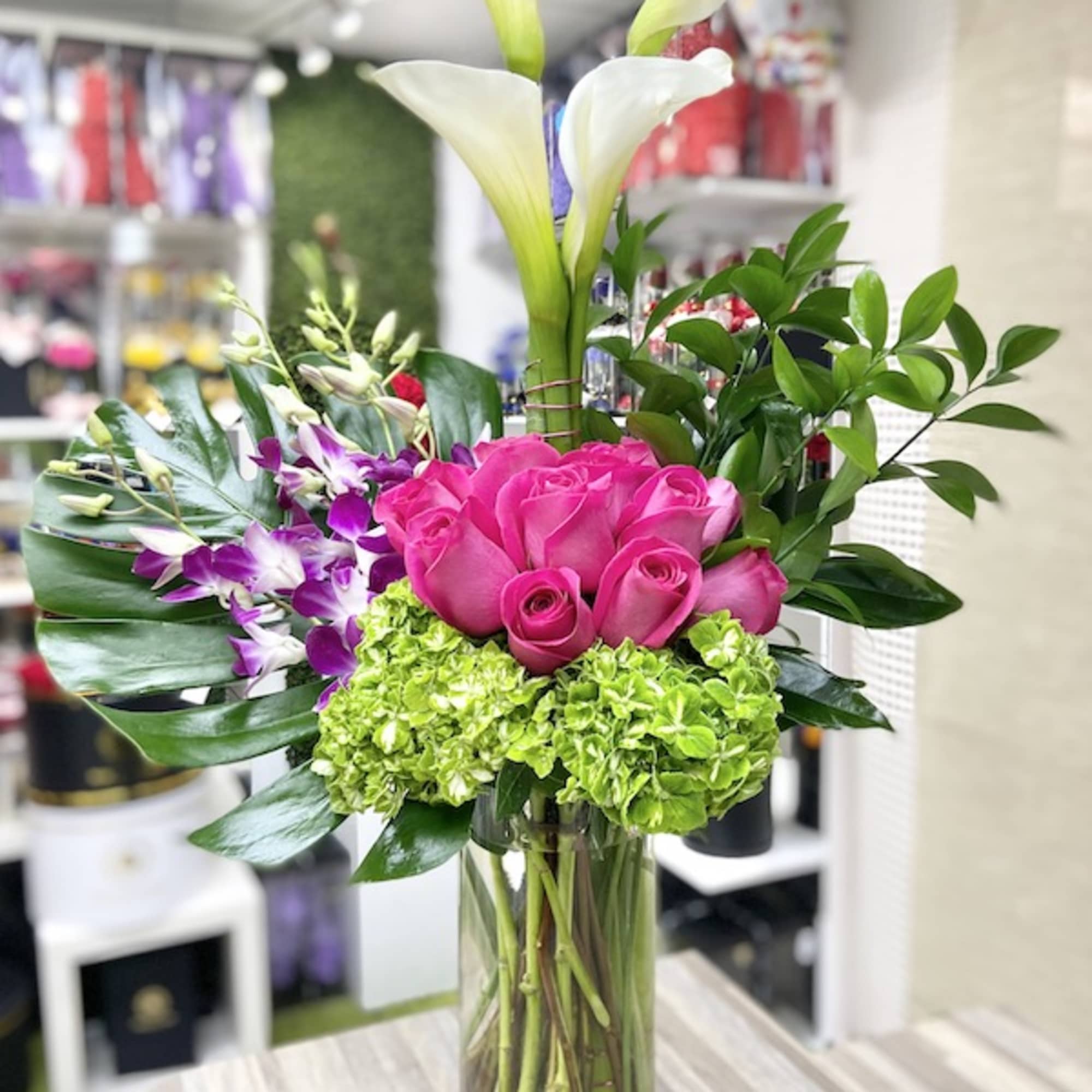 Tall arrangement with white calla lilies, pink roses, purple orchids, and green hydrangea in a glass vase