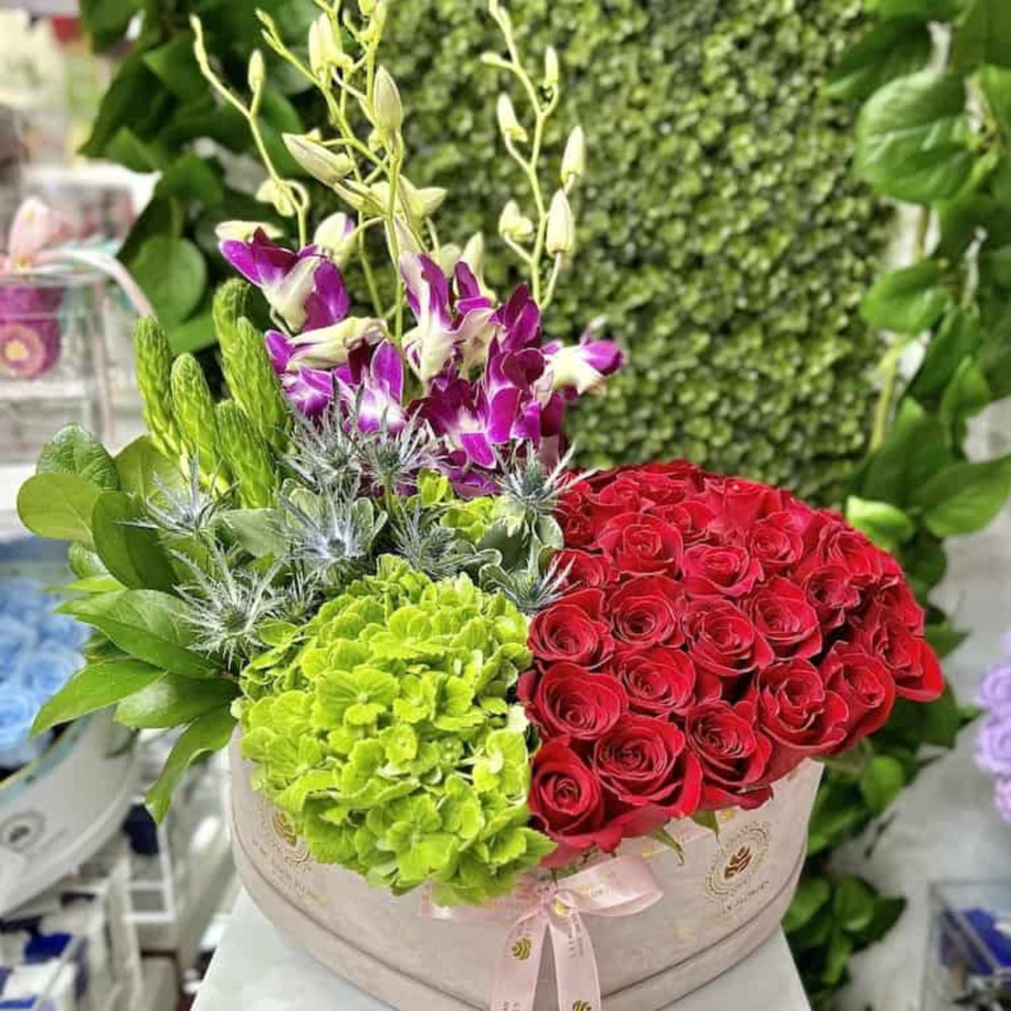 Round hatbox arrangement with red roses, green hydrangeas, and purple orchids, photo 3 of 4