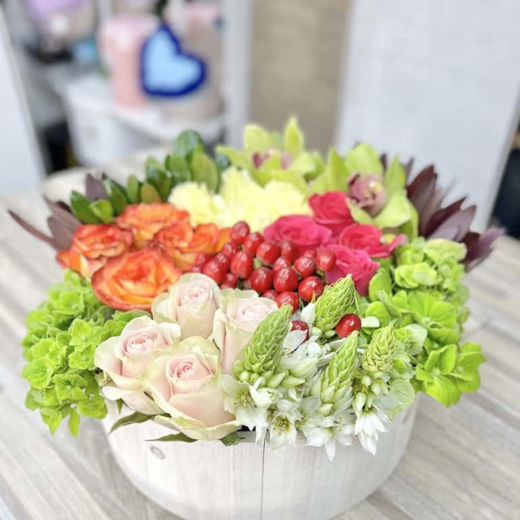 Low round arrangement of pink and orange roses, green hydrangeas, berries, and white blooms in a white wooden container