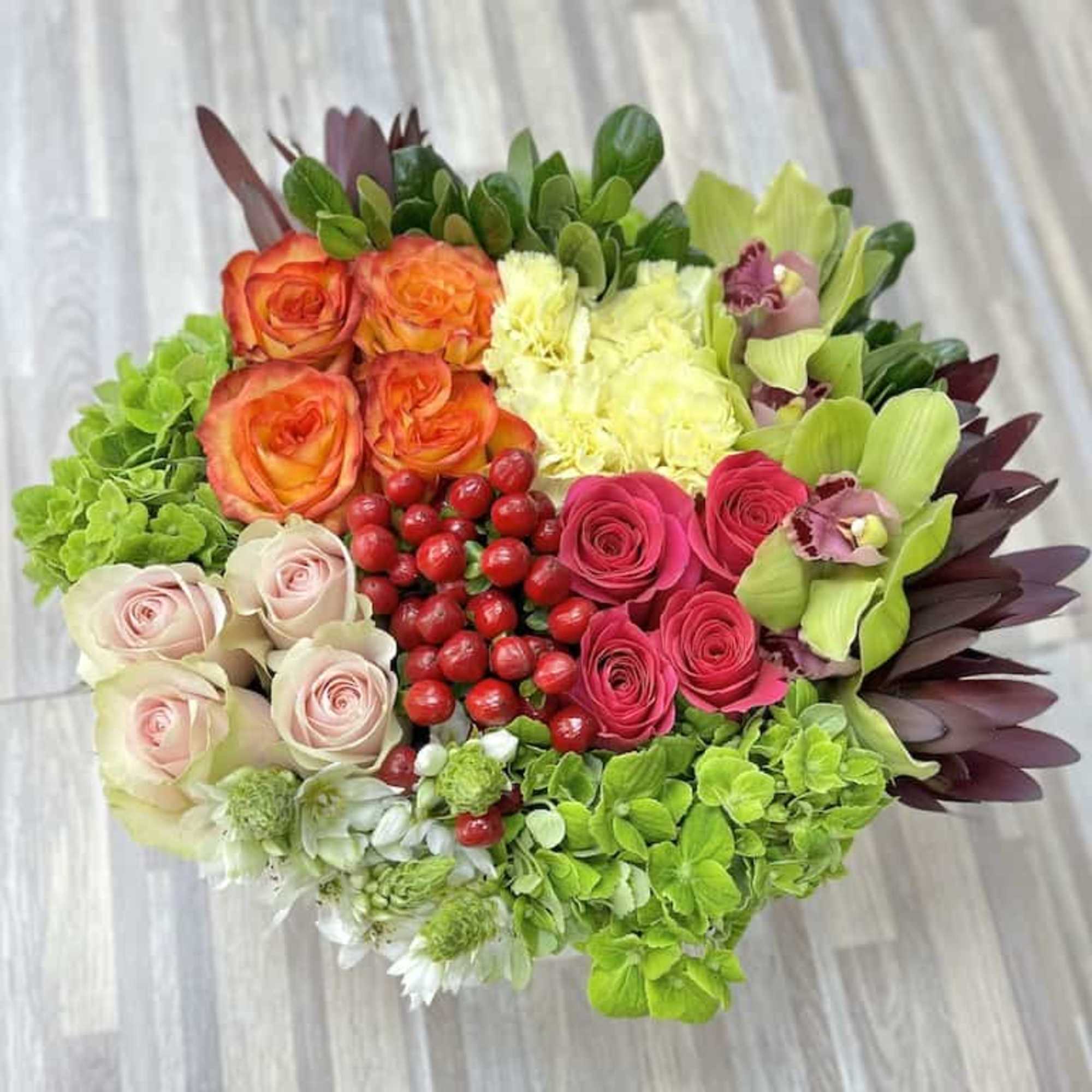 Round arrangement of green hydrangeas, mixed roses, orchids, carnations, and red berries in bright colors