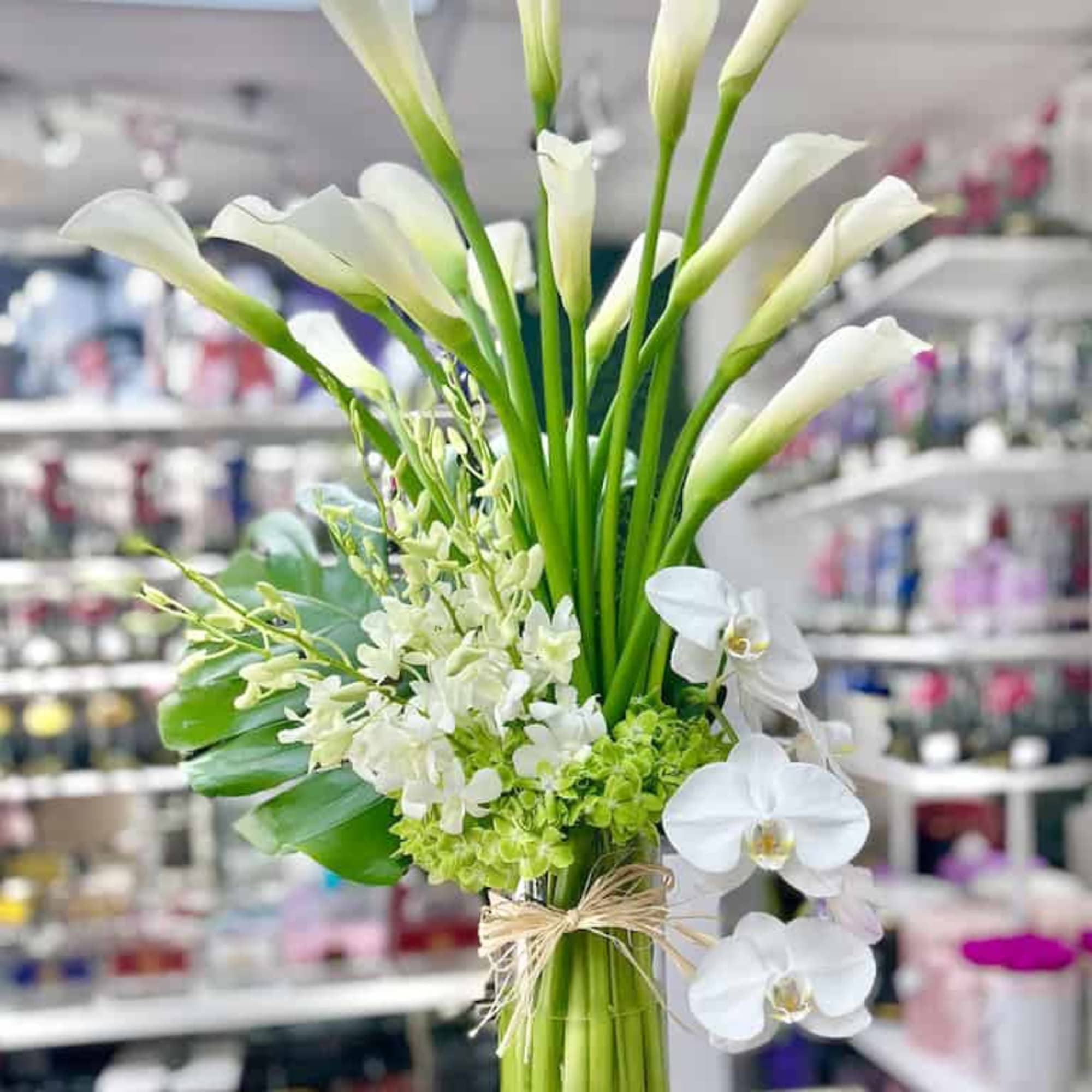 Tall arrangement of white calla lilies and orchids in a clear glass vase