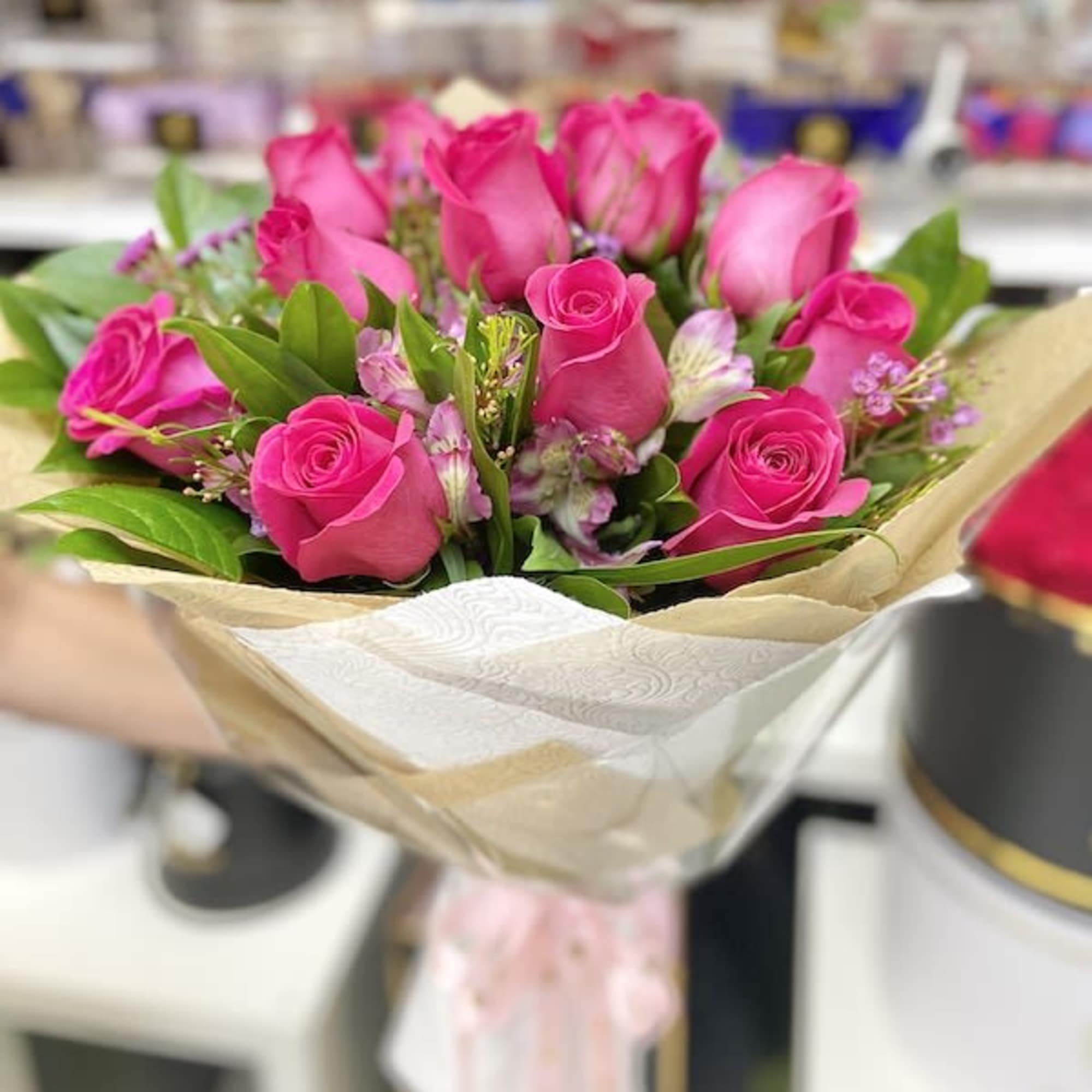 Hand-tied bouquet of bright pink roses wrapped in patterned paper and ribbon.