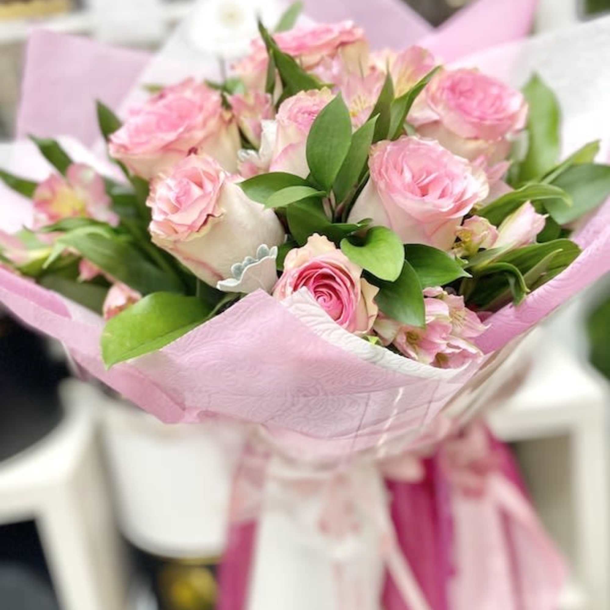 Hand-tied bouquet of pink roses wrapped in pink patterned paper with ribbon.