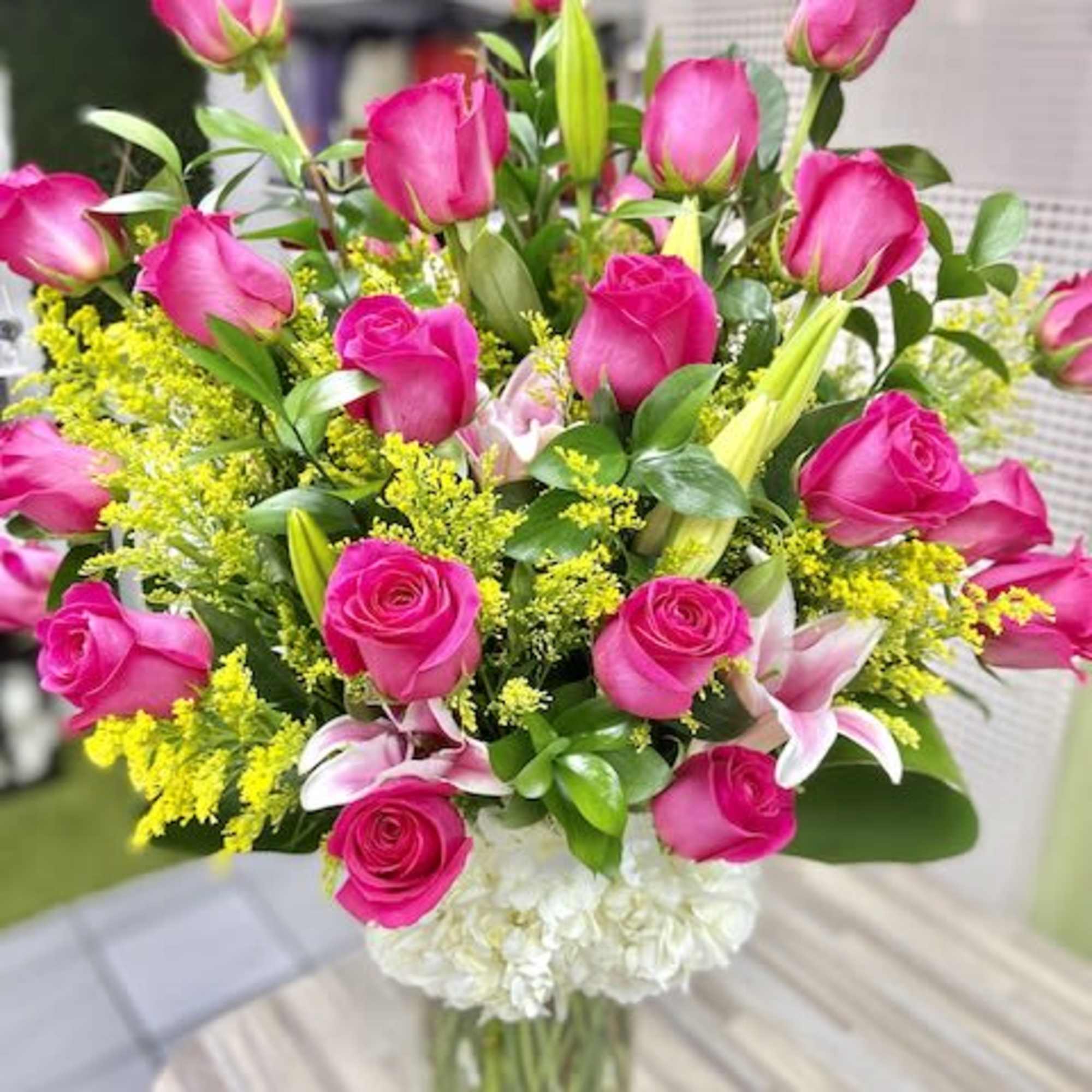 Tall arrangement of hot pink roses, pink lilies, yellow filler, and white hydrangeas in a clear glass vase