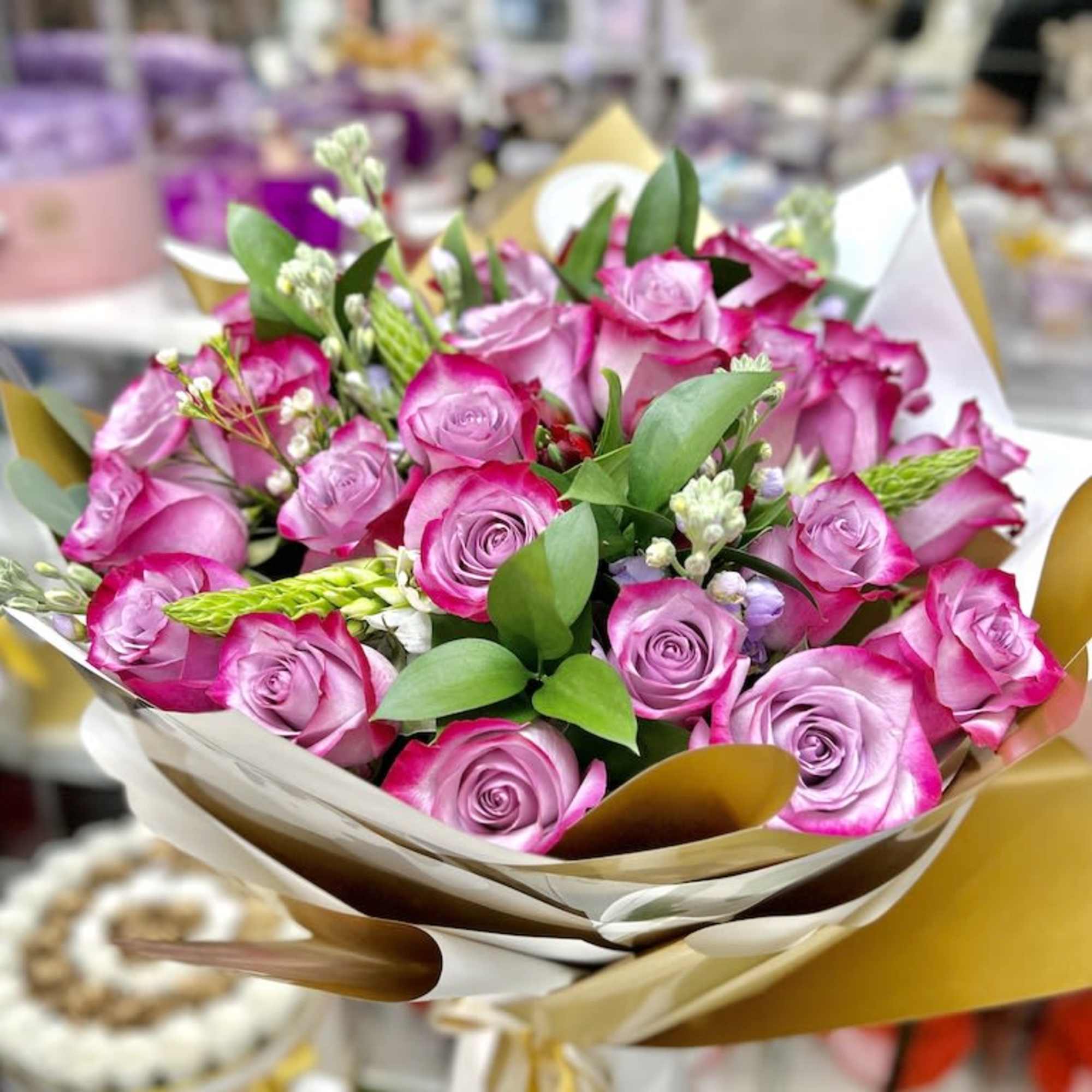 Hand-tied bouquet of pink roses with white accent flowers in cream and gold wrapping