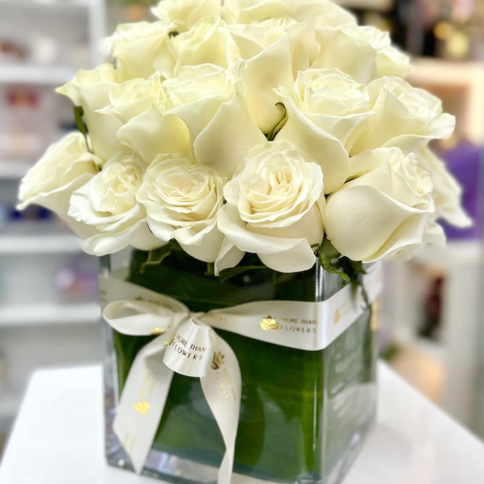 Compact arrangement of cream roses in a square glass vase wrapped with a white ribbon
