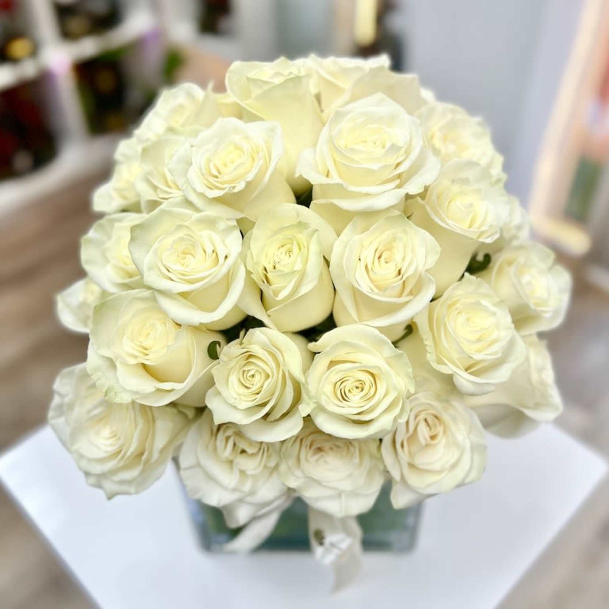 Compact arrangement of ivory roses in a clear glass cube vase