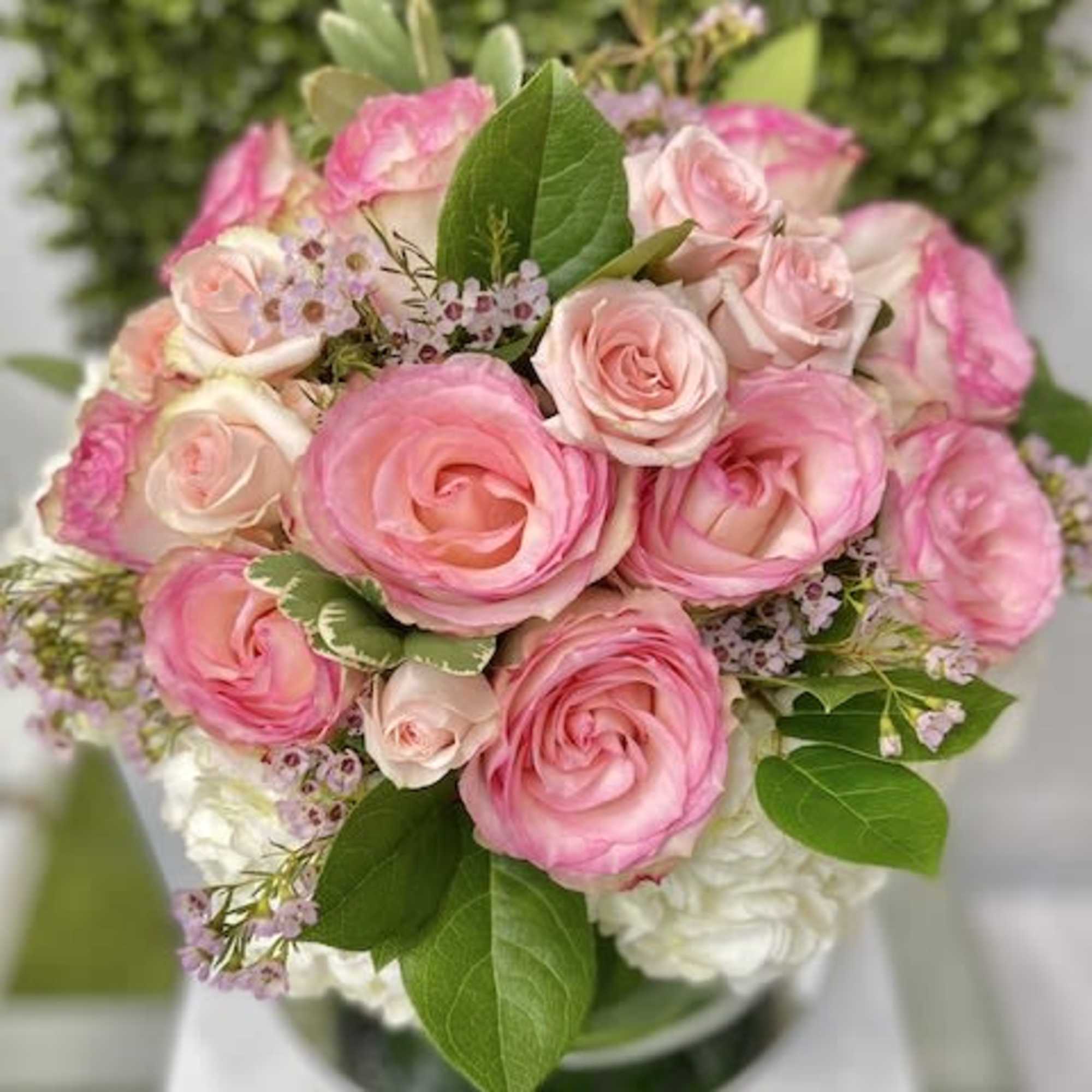 Round arrangement of pink roses with white blooms in a clear glass vase