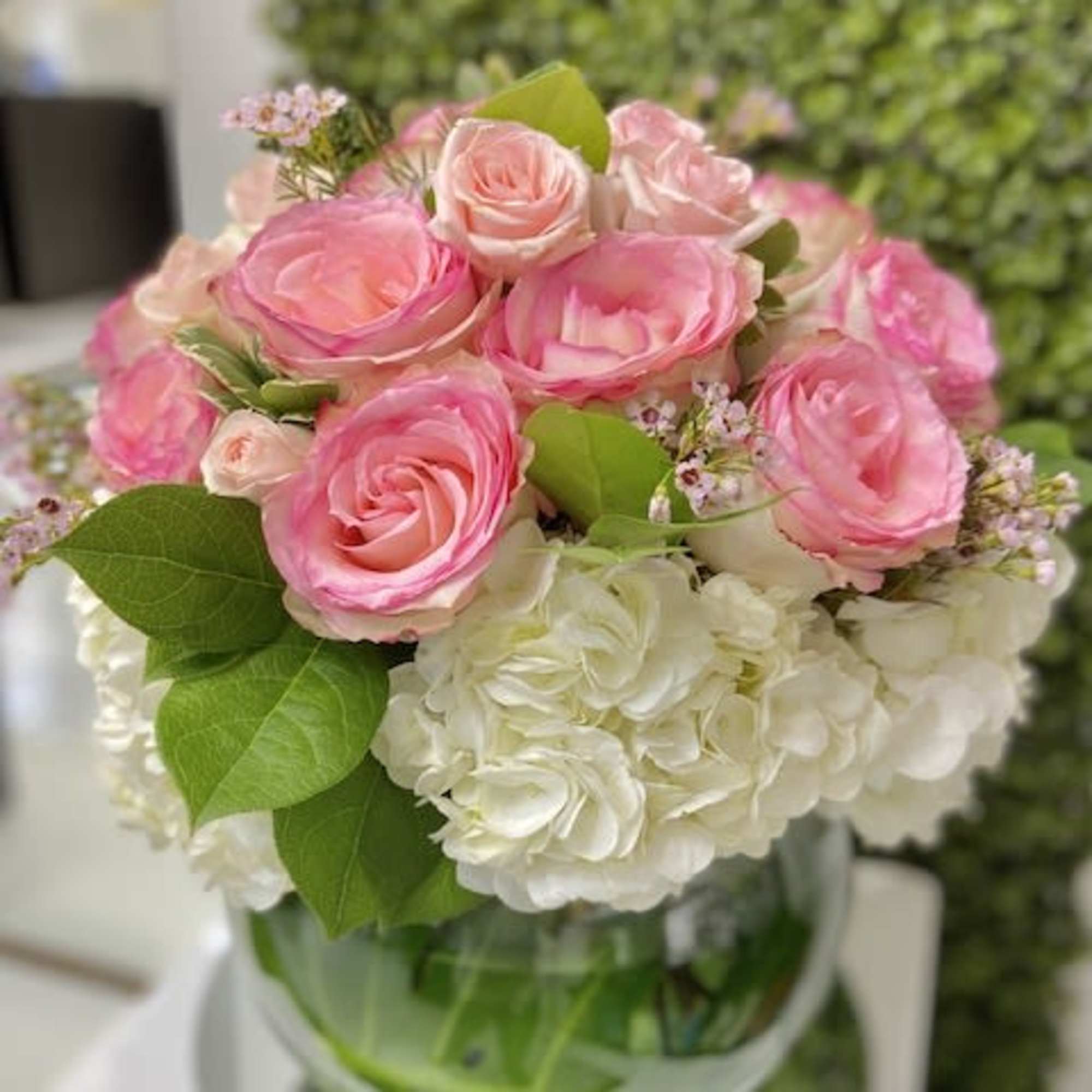 Round arrangement of pink roses and white hydrangeas in a clear glass bowl vase