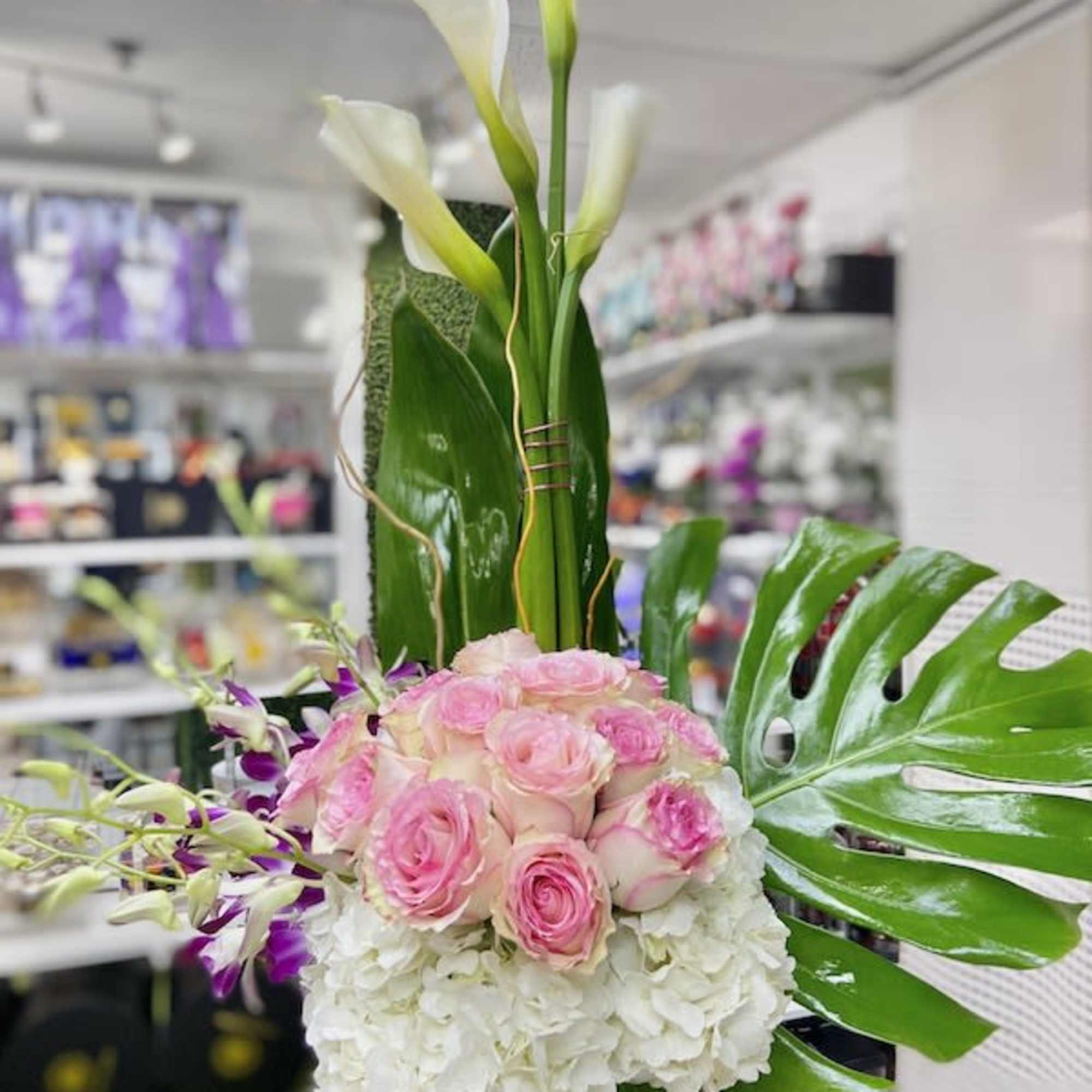 Tall arrangement with white calla lilies, pink roses, orchids, and hydrangeas in a glass vase