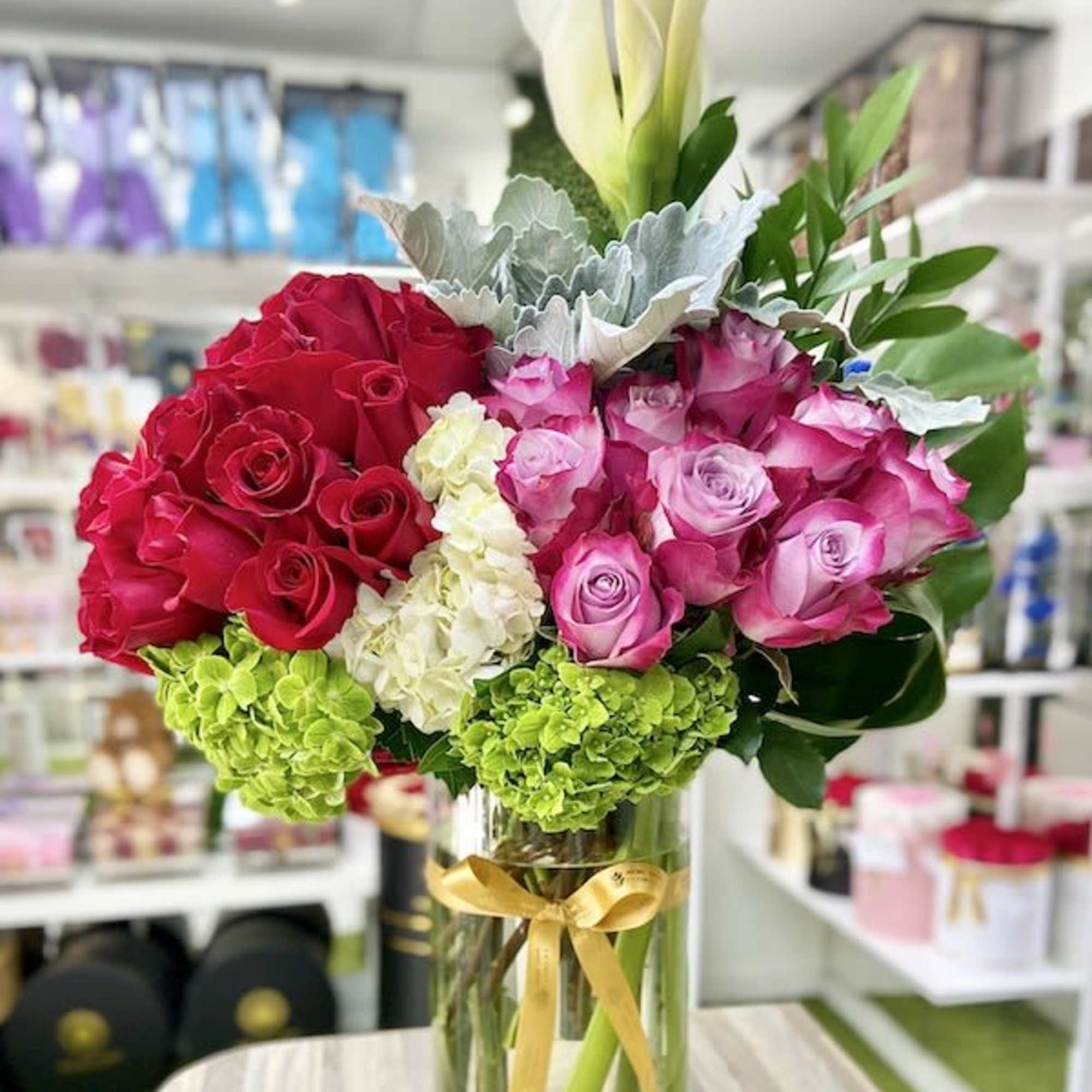 Tall glass vase with red and pink roses, green hydrangeas, and white calla lilies.