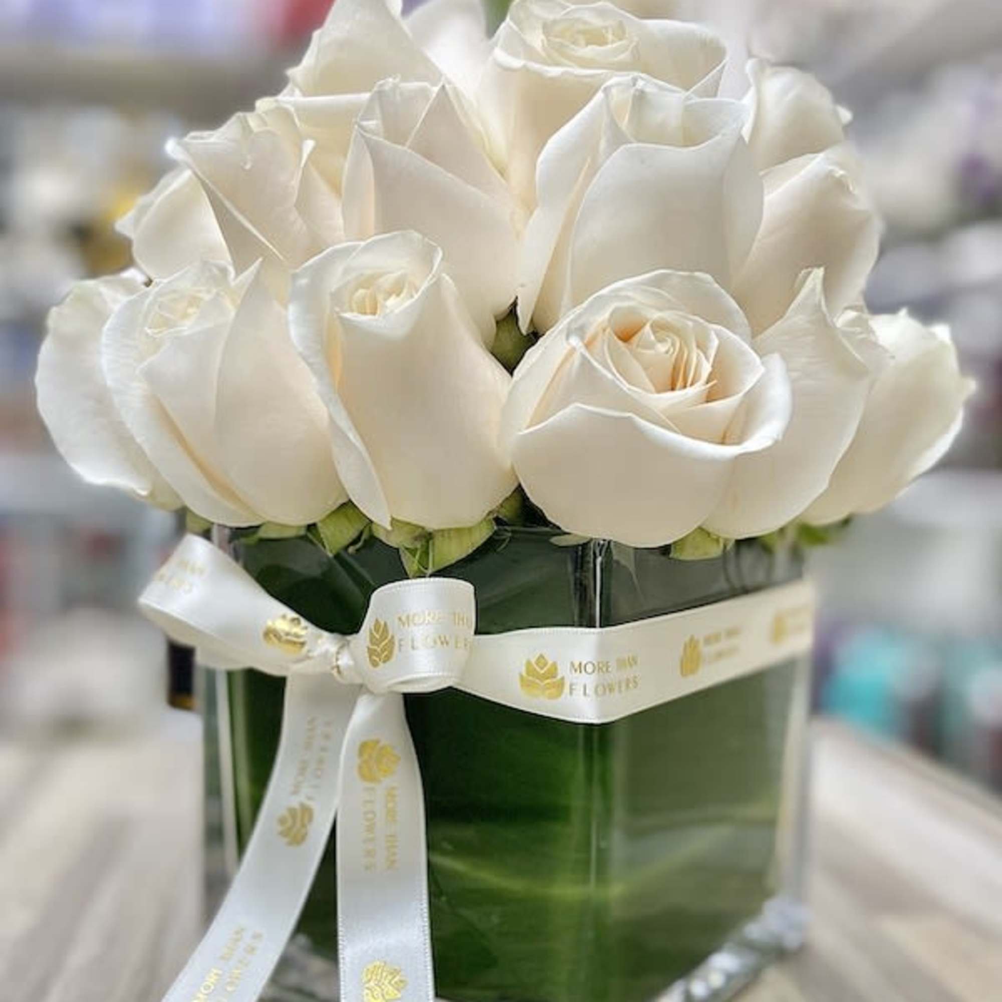 Compact arrangement of white roses in a square glass vase with a white ribbon bow