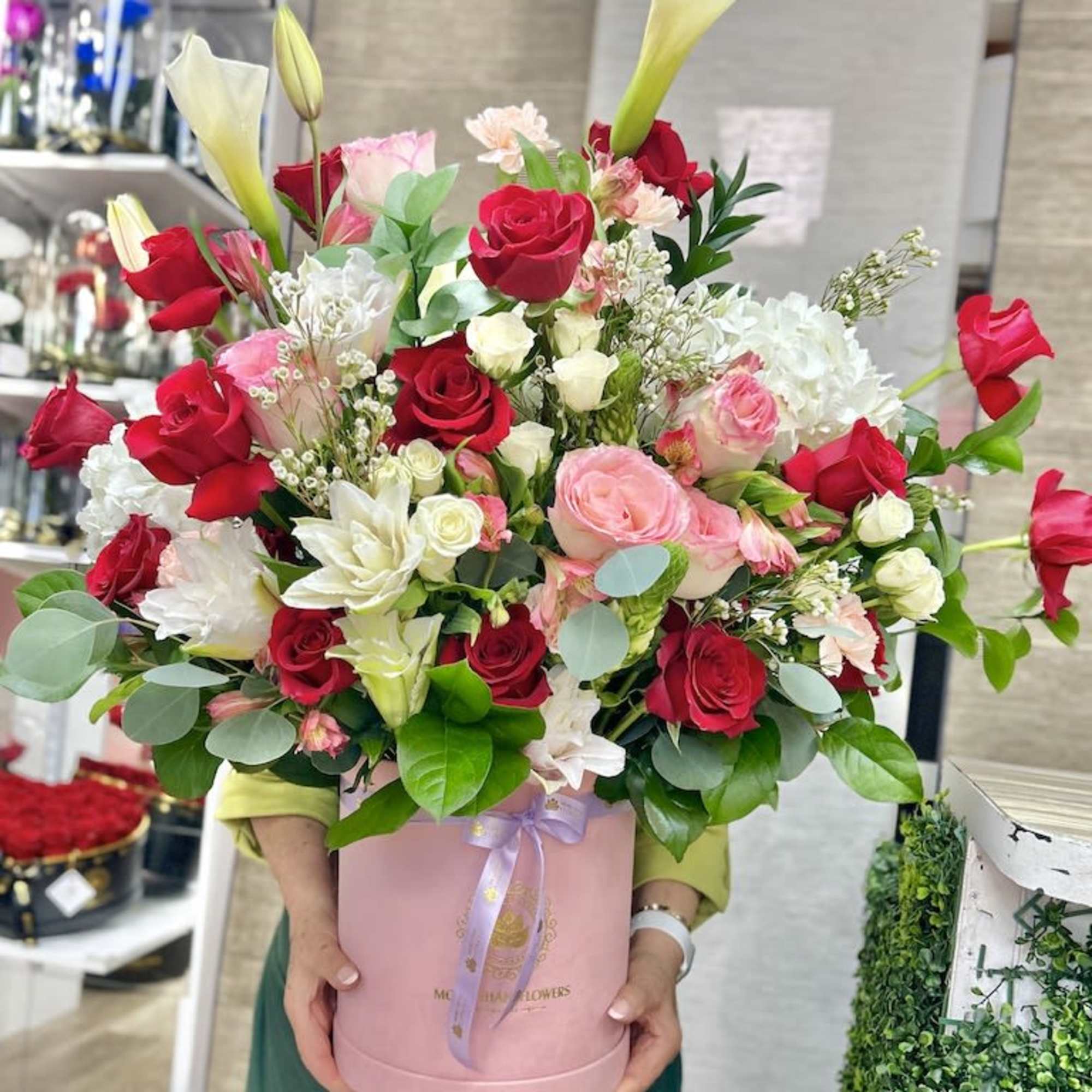 Large arrangement of red and pink roses with white calla lilies in a pink hat box.