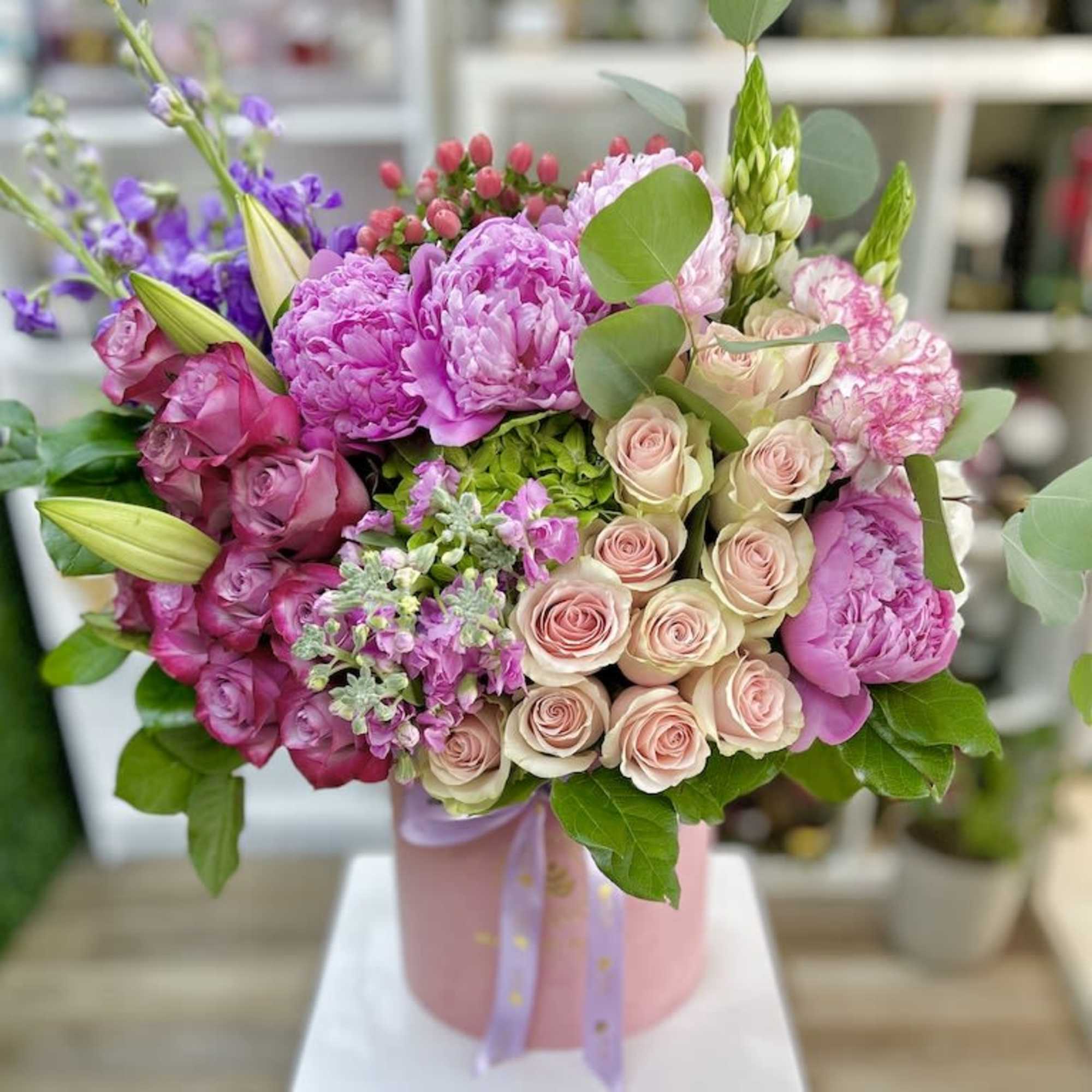 Lush arrangement of pink peonies, roses, and mixed blooms in a pink hatbox with ribbon