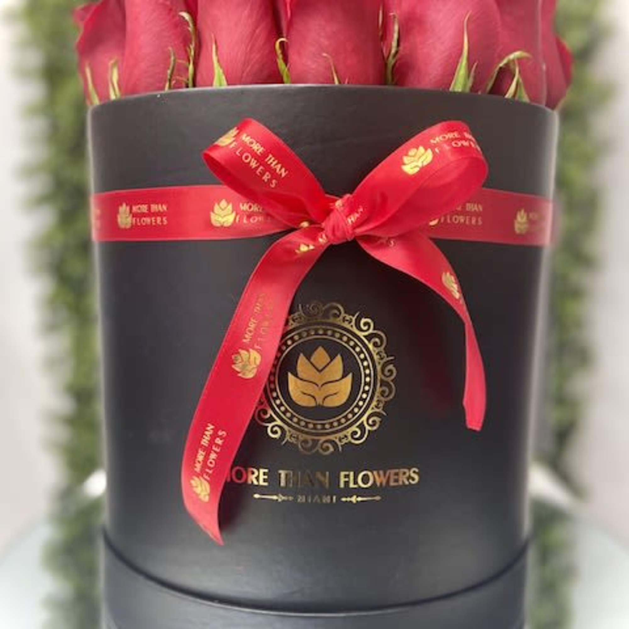 Round black hatbox filled with red roses and tied with a red ribbon bow