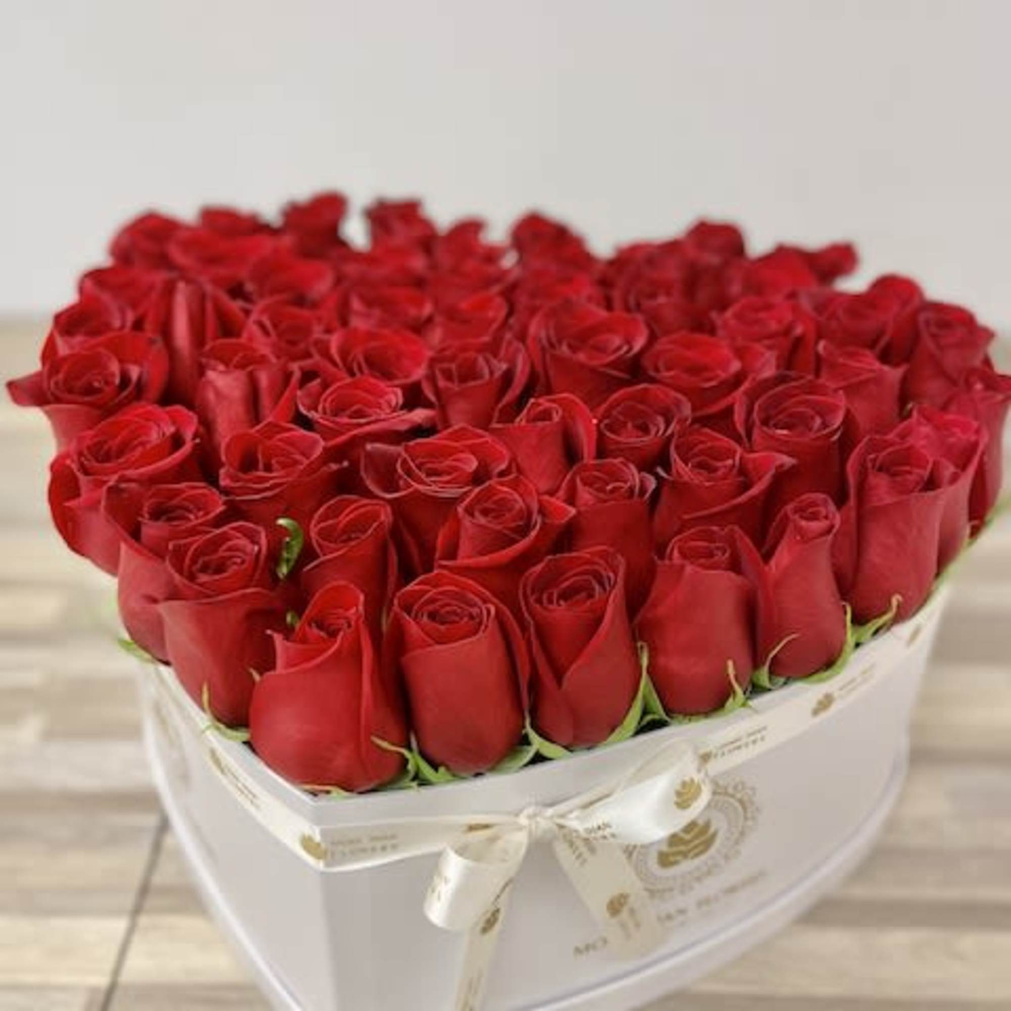 Heart-shaped white box filled tightly with red roses and tied with a cream ribbon