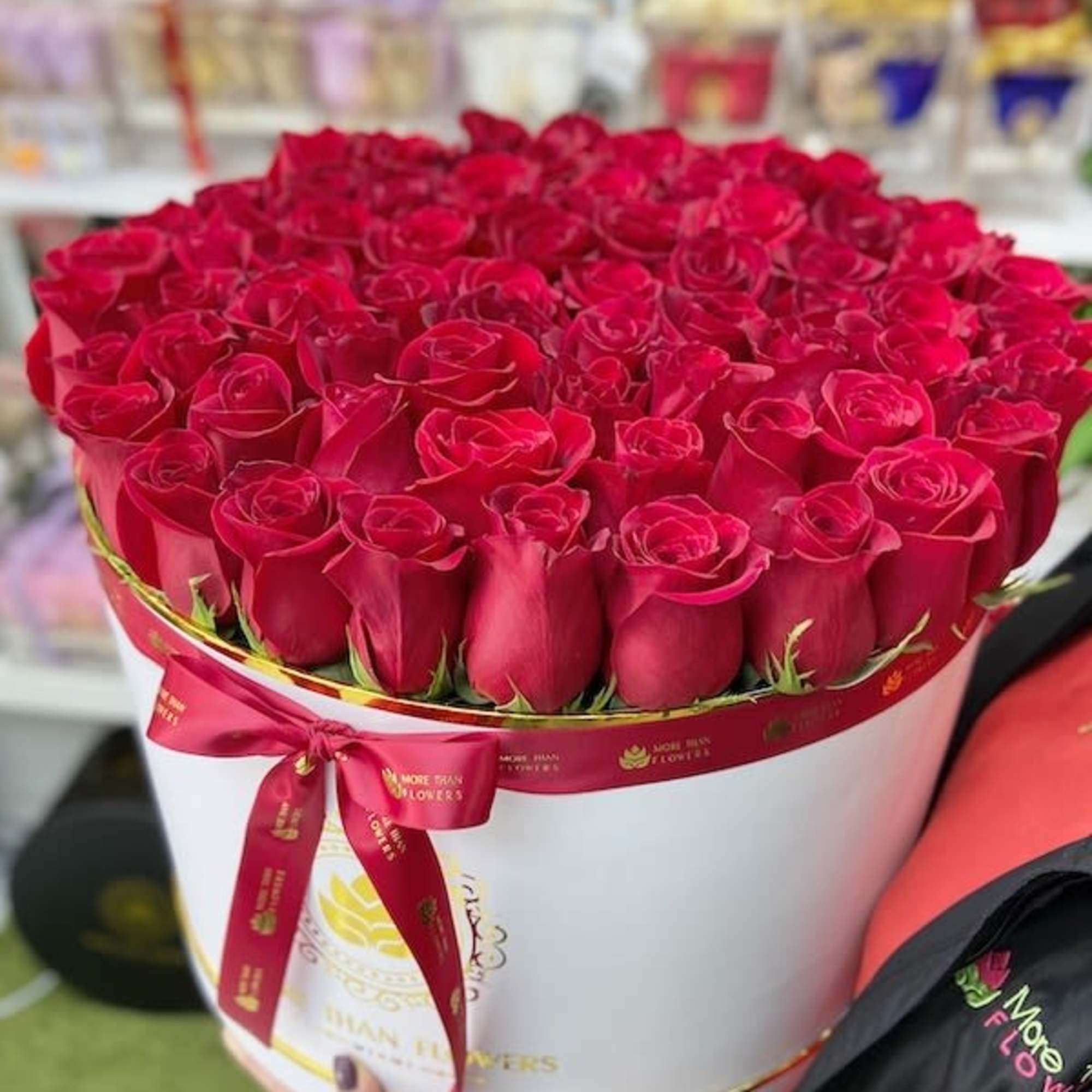 Large round box filled with tightly packed red roses, wrapped with a red ribbon