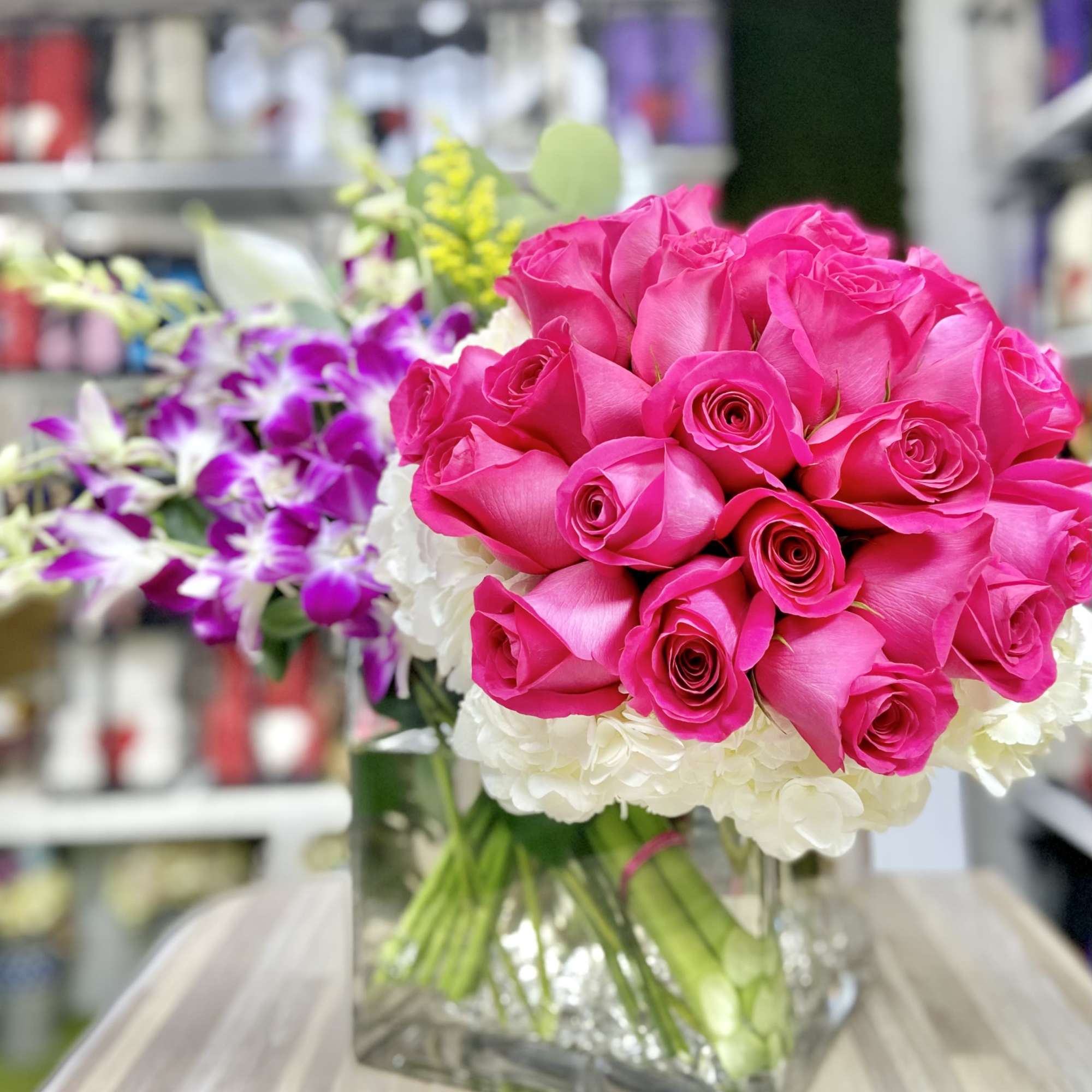 Square vase of hot pink roses with white hydrangeas and purple orchids.