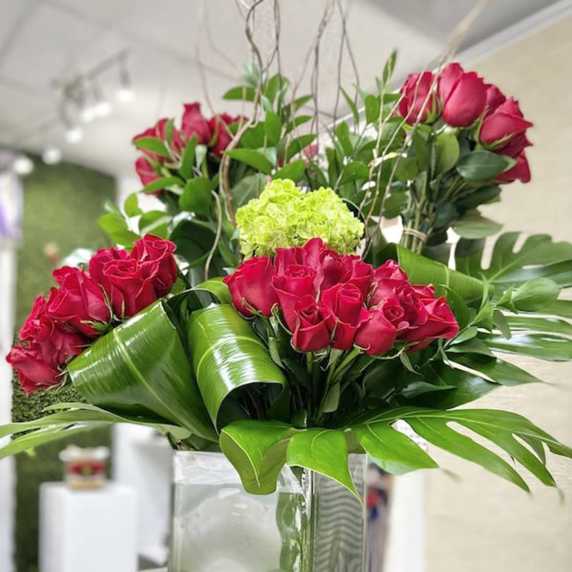 Tall arrangement of red roses with green hydrangea in a clear glass cube vase