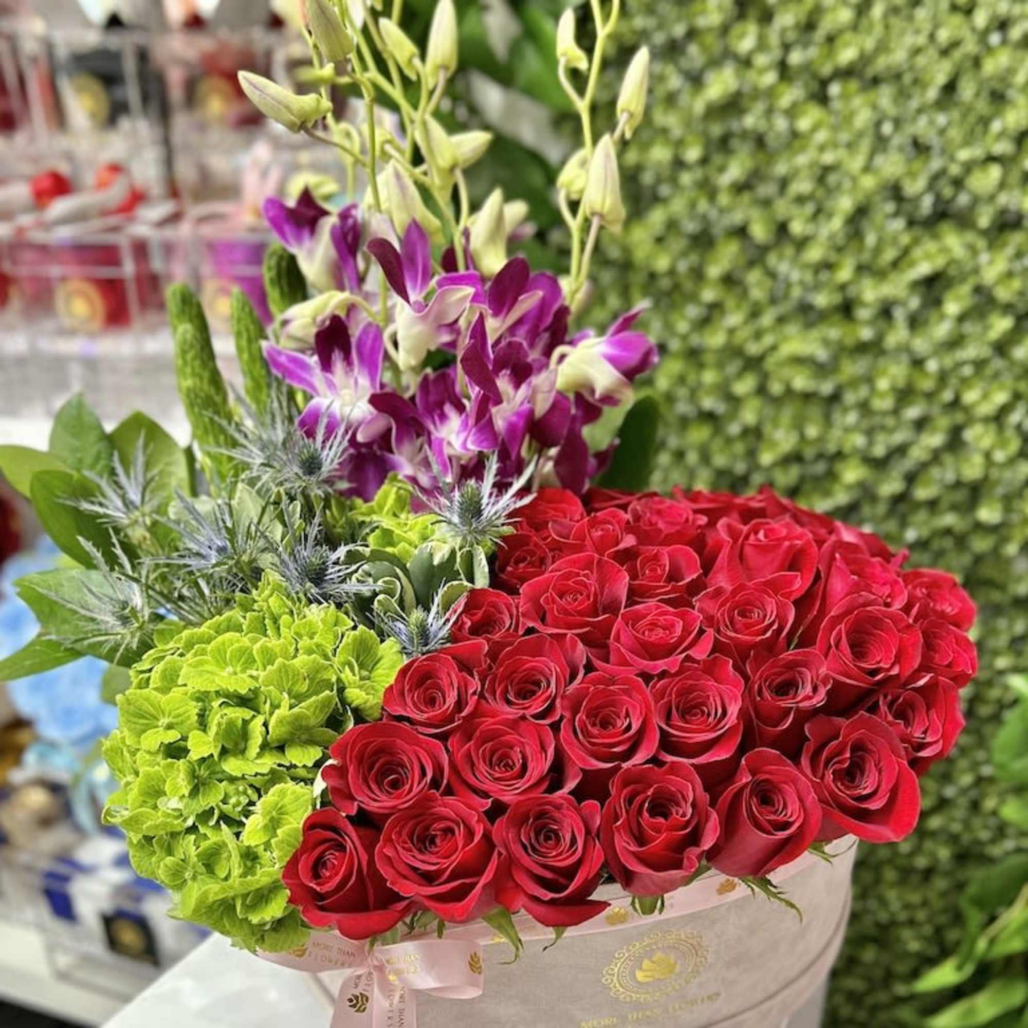 Round hatbox arrangement with red roses, green hydrangeas, and purple orchids