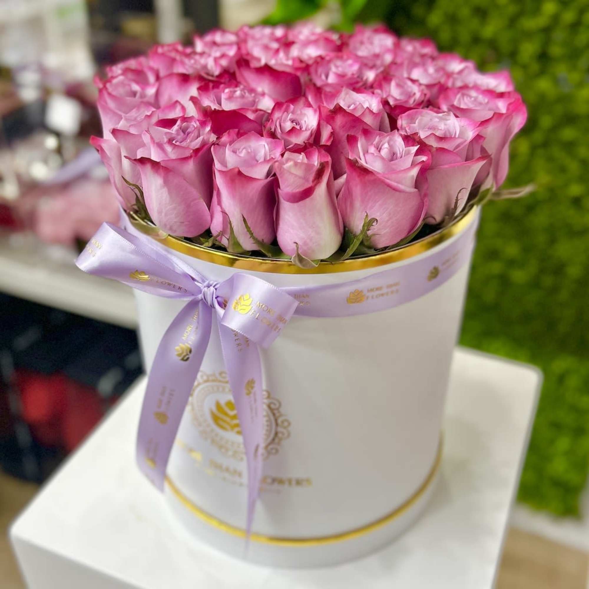Round white hatbox filled with pink roses and tied with a lavender ribbon bow